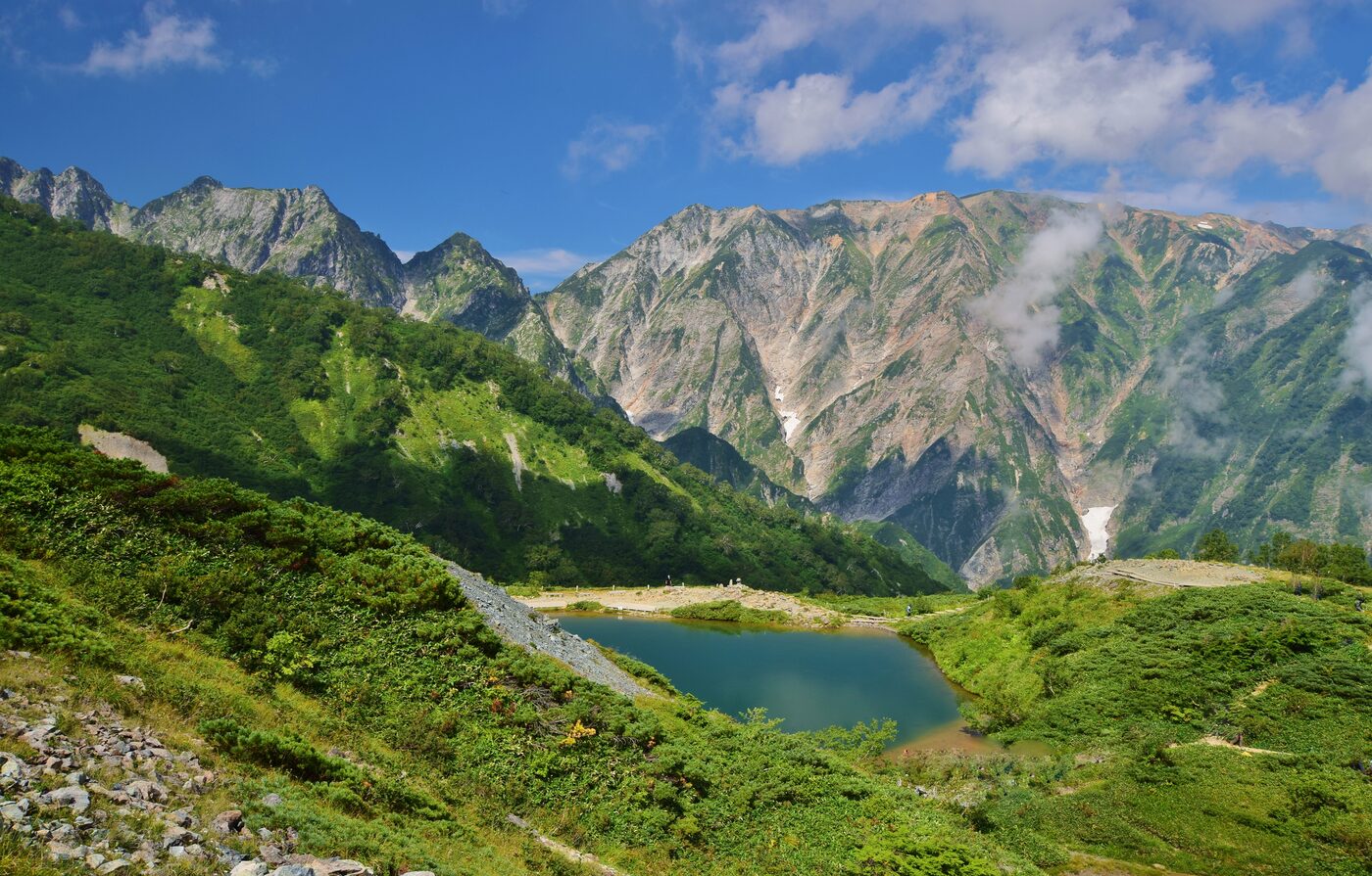 Happo-ike alpine pond surrounded by green slopes and rocky peaks in summer