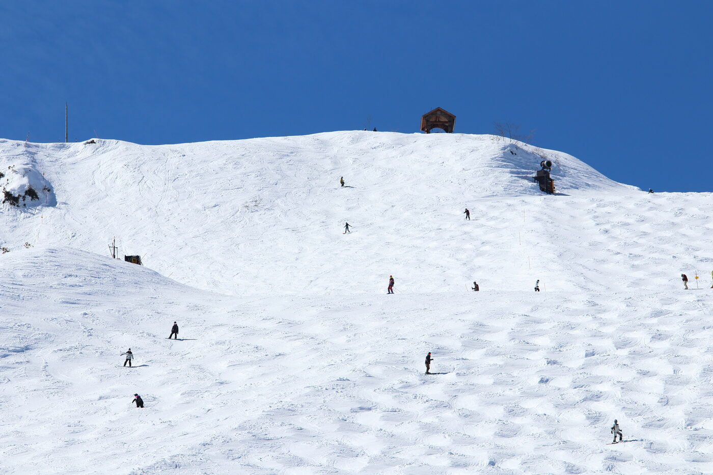 Hakuba Happo-One ski slope with multiple skiers descending a wide snow run on a sunny winter day