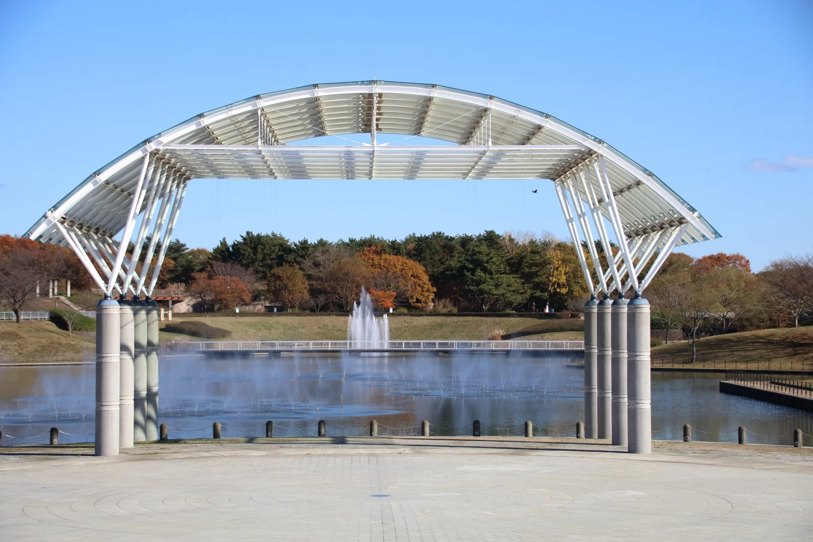 Fountain and arched pavilion at Hitachi Seaside Park in late autumn with surrounding trees in subtle russet color — the park's quiet November transition window