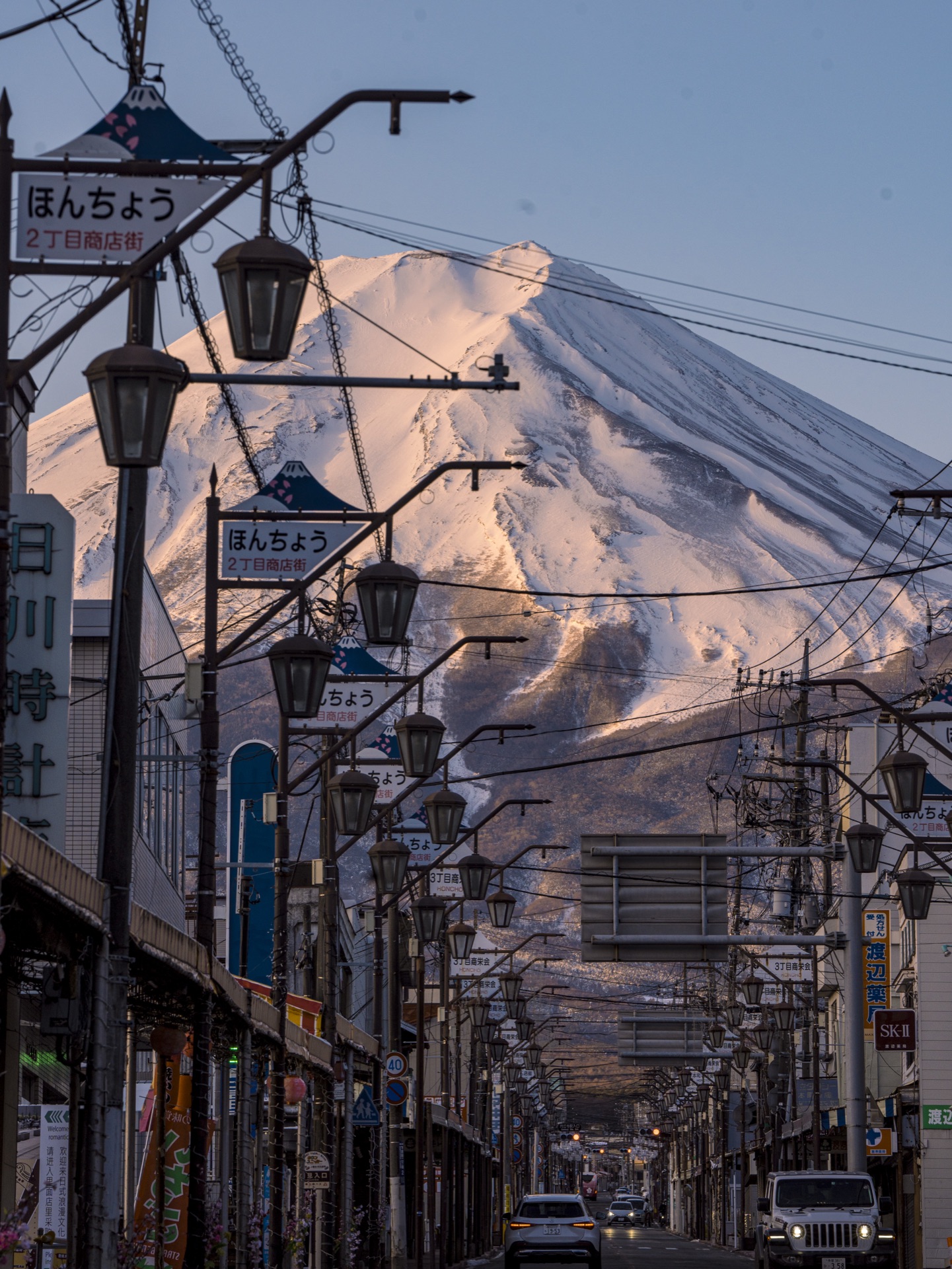 Vertical composition of Mt Fuji at the end of Honmachi 2-chome retro shopping street with overhead wires and lampposts