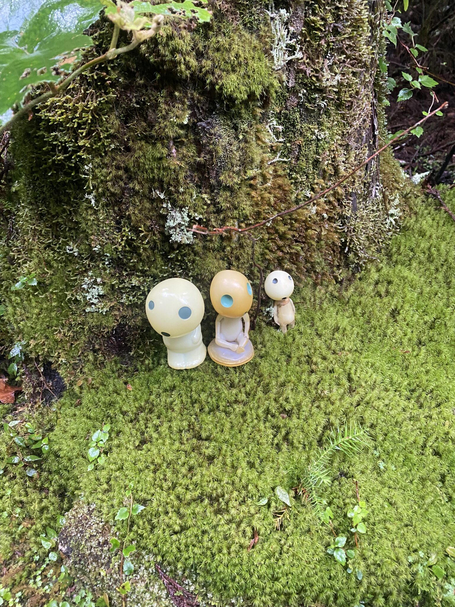 Three small Kodama spirit figurines on a mossy cedar log