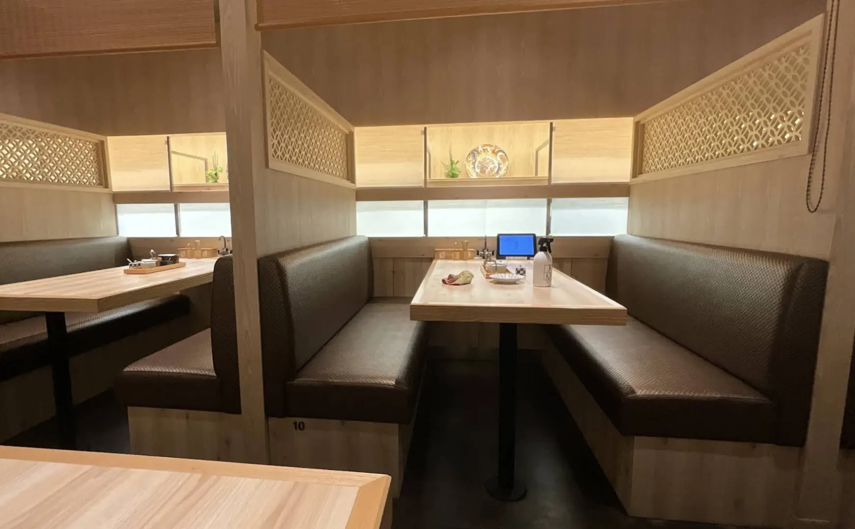 Private booth interior at Kaishinmaru Fukuoka — leather banquettes, blond wood tables, traditional Japanese latticework panels above the seats, with the next booth visible in the background