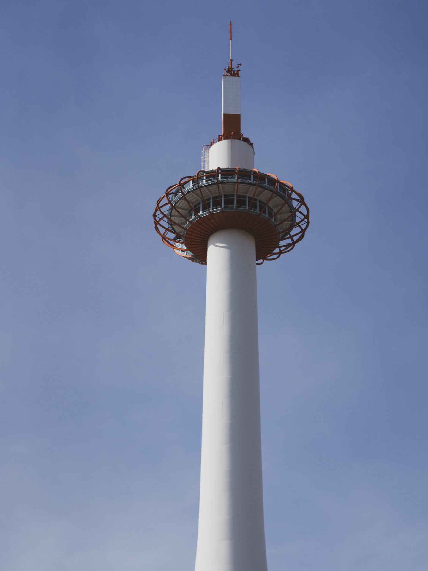 The white slim shaft of Kyoto Tower rising vertically into a clear sky with the orange observation deck ring at the top