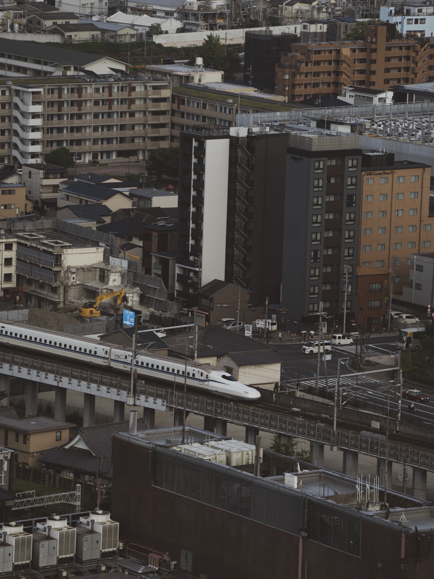 A white Shinkansen train passing through the city grid as seen from the Kyoto Tower observation deck