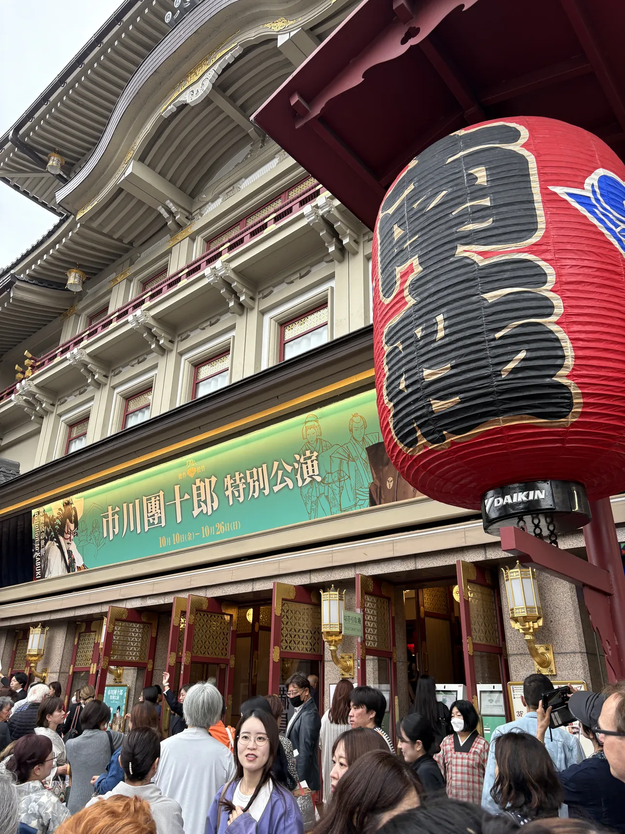 Large red lantern hanging at Minamiza entrance with the Ichikawa Danjuro XIII special performance poster in green during daytime
