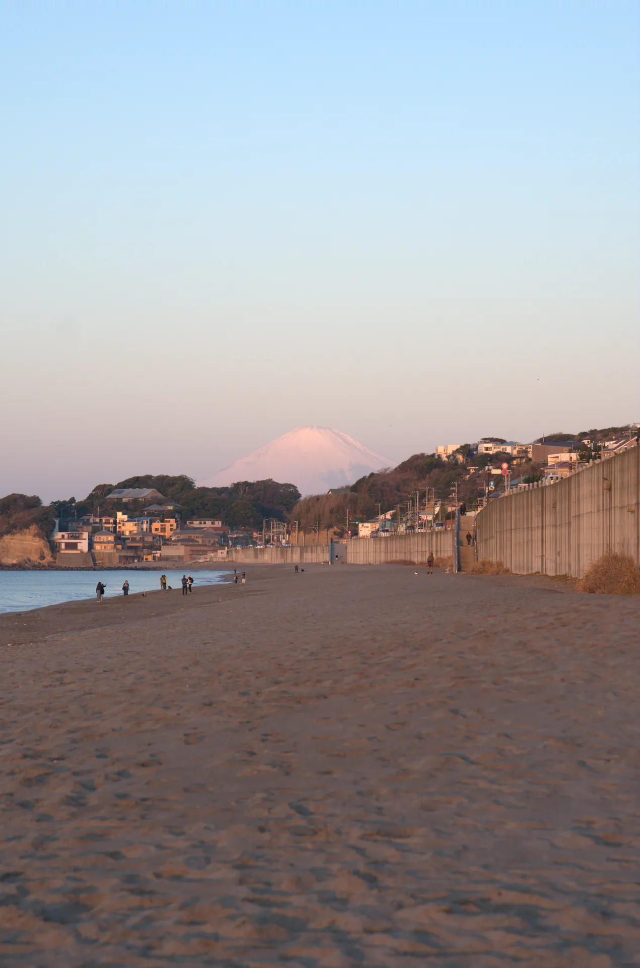 Mt Fuji visible across the bay from Shichirigahama beach in Shonan with people walking on the sand at dawn