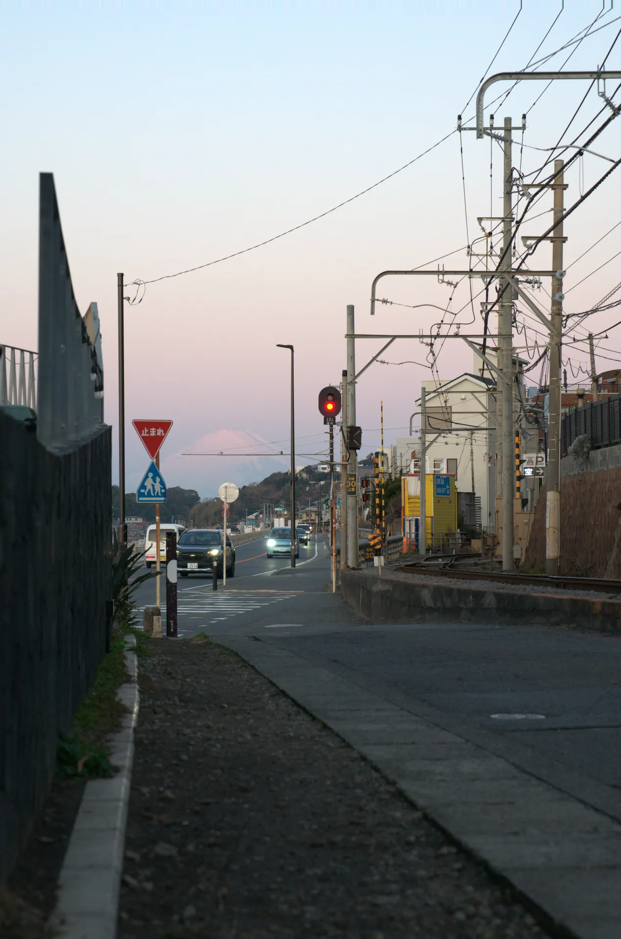 Mt Fuji silhouetted in pink dawn light from a Shonan street with traffic signals and Enoshima Electric Railway crossing in the foreground
