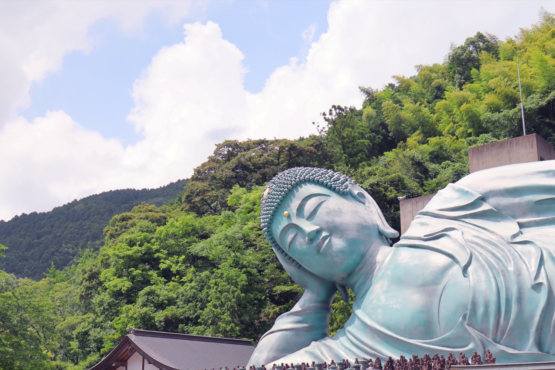 The Buddha's face viewed against the green Sasaguri mountain backdrop with summer clouds