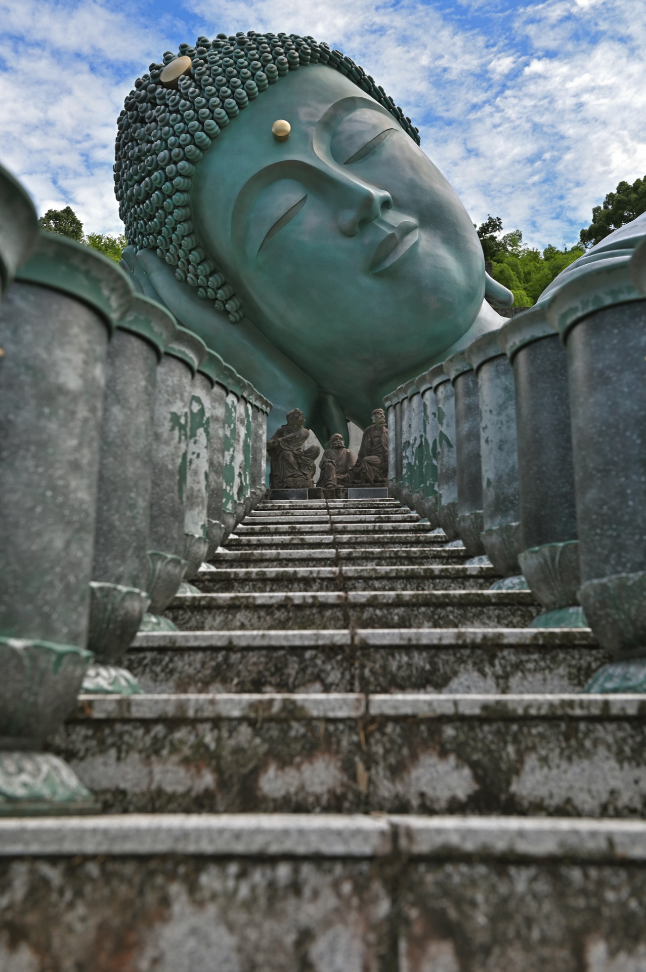 Looking up the stone stairs toward the Reclining Buddha's head with two small disciple figures visible at the top of the climb