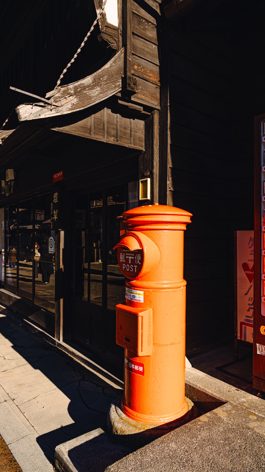 A vintage cylindrical red Japanese postbox standing on the main street of Naraijuku in winter sunlight
