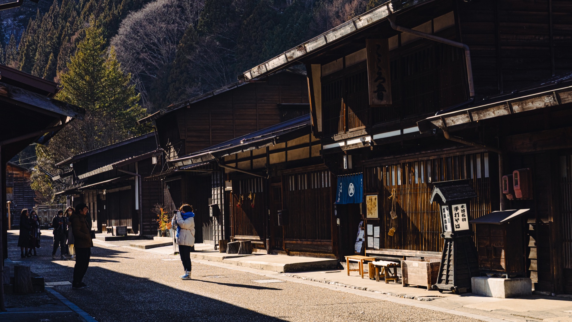 Locals walking down the empty winter street of Naraijuku in the morning sun with shadows from the wooden eaves