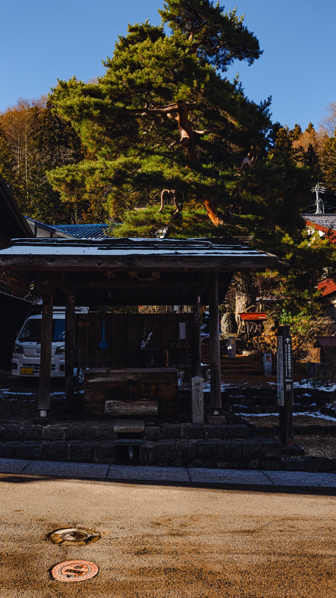 The chozuya purification basin at Shizume Shrine with an old pine tree behind it under a blue winter sky