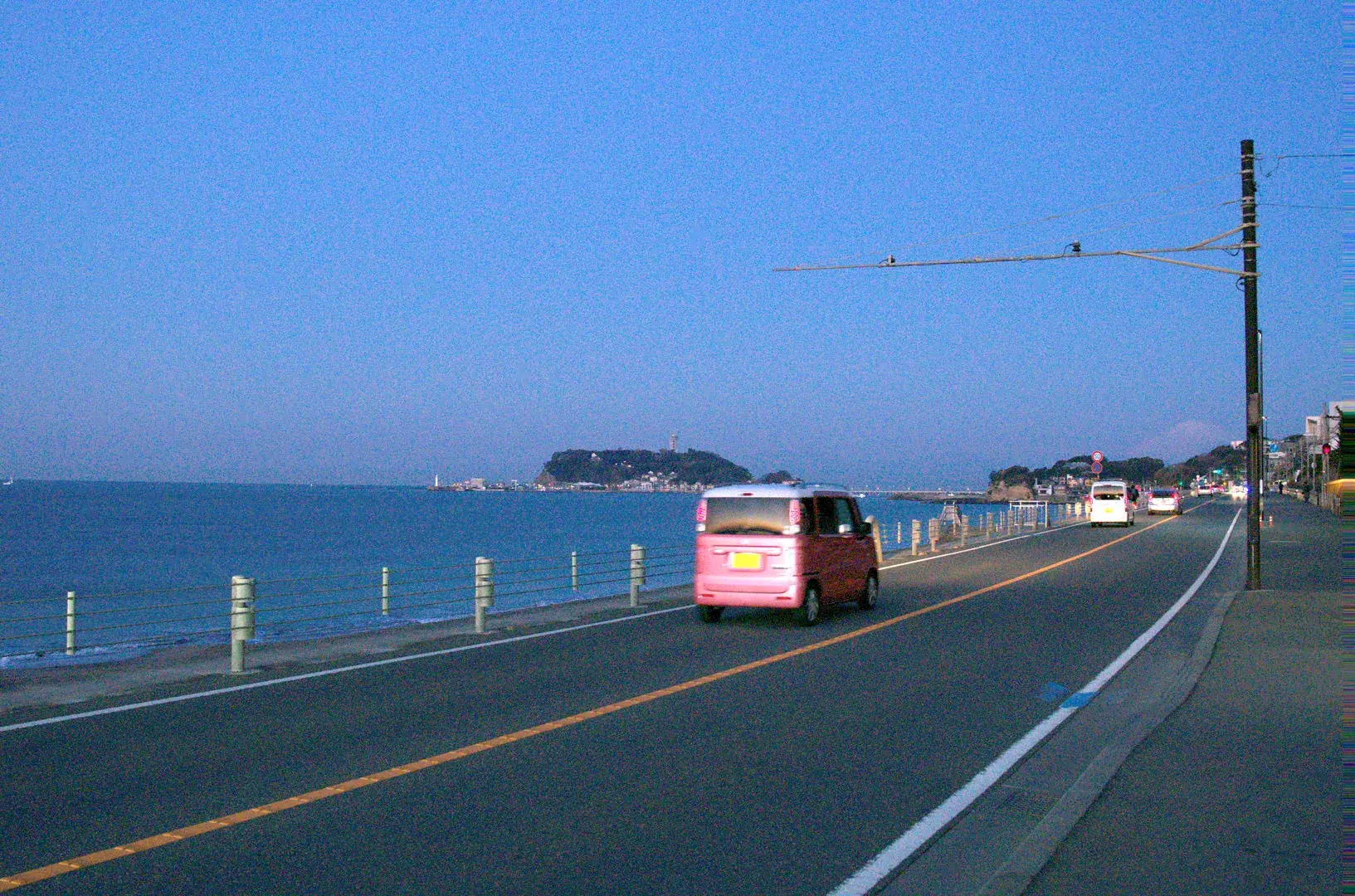 The Shonan coast road heading toward Enoshima island in the morning with a small pink delivery van and Enoshima visible in the distance