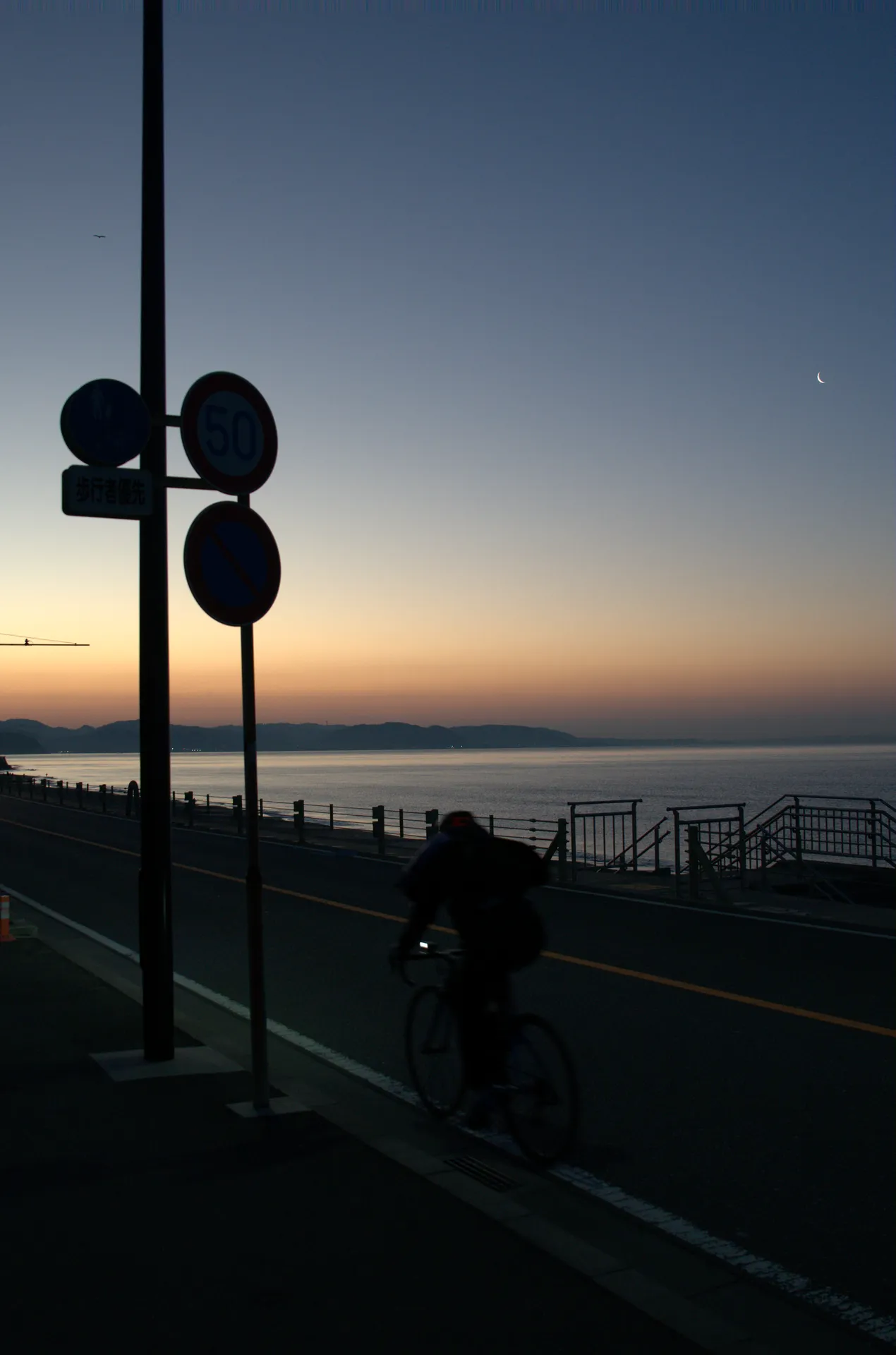A cyclist silhouetted against the Shonan sunrise riding past traffic signals on the coast road