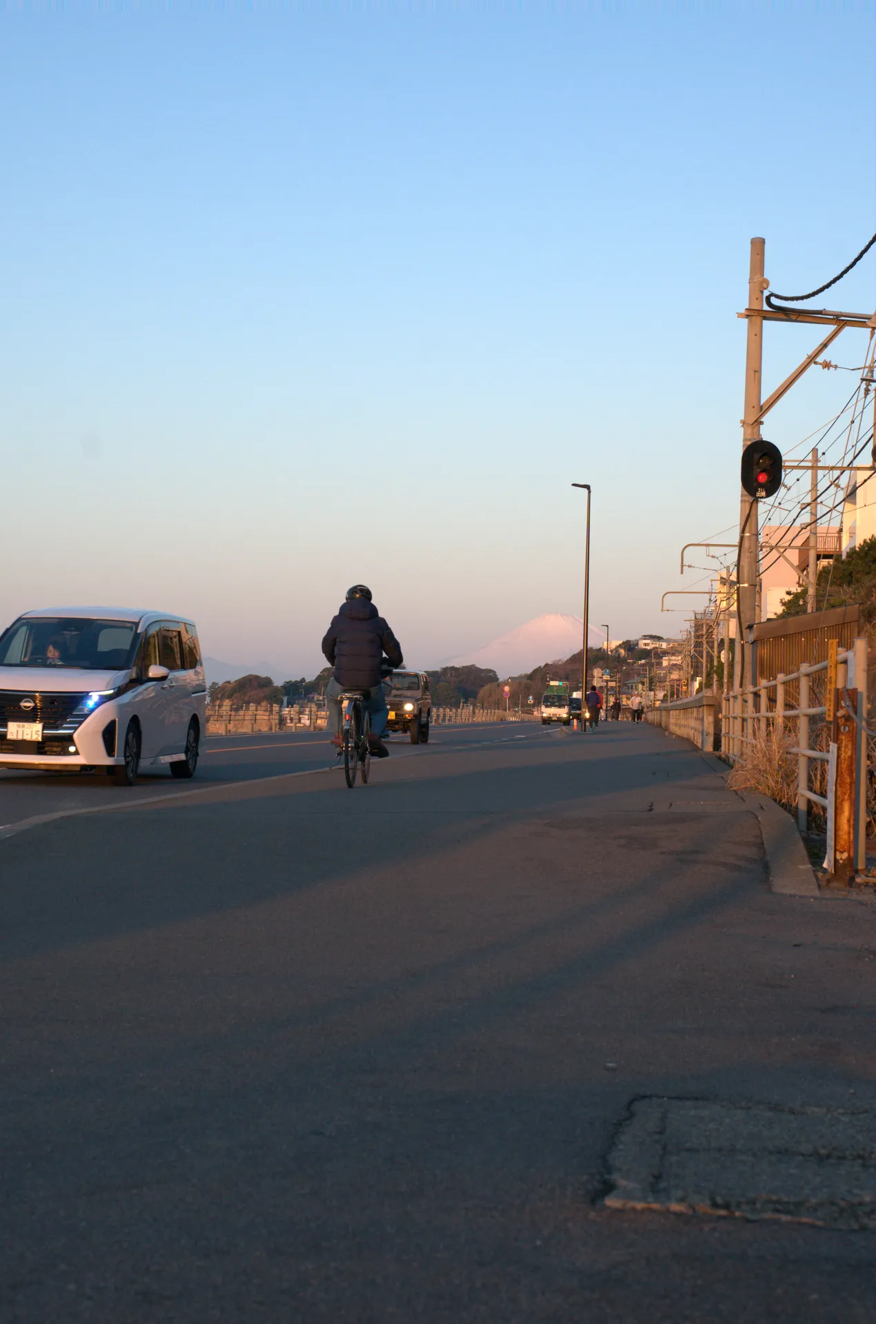 Morning cyclist on the Shonan coast road with Mt Fuji visible in the distance under early sunlight