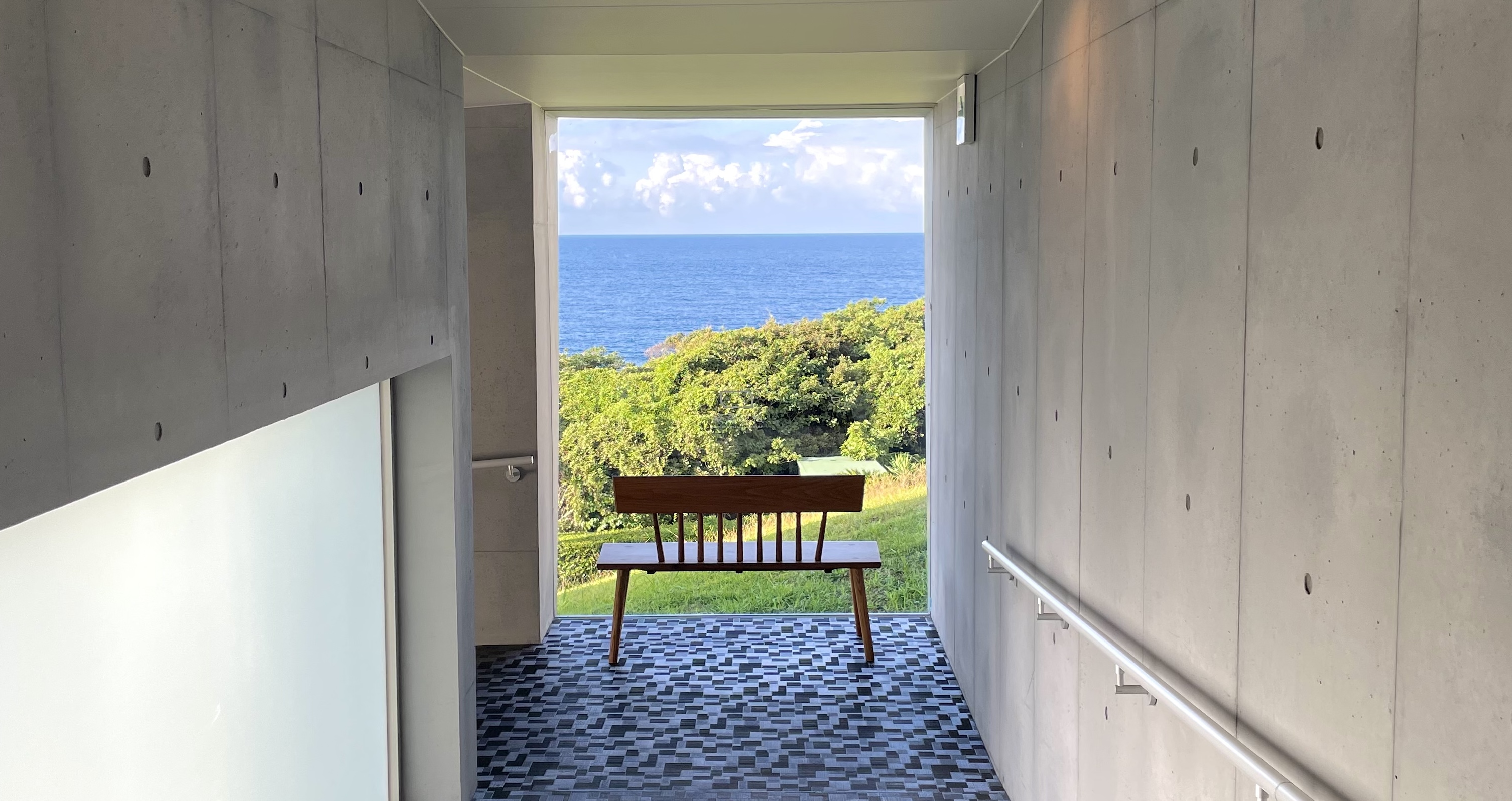 Concrete corridor at THE HOTEL YAKUSHIMA framing the Pacific Ocean view with a wooden bench