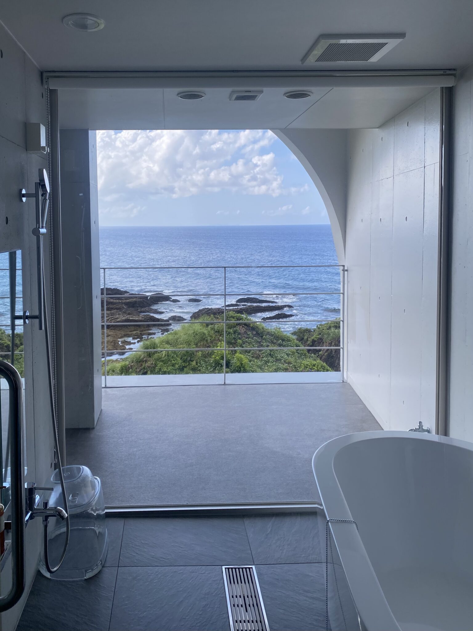 Freestanding bathtub at THE HOTEL YAKUSHIMA with a full-height arch window opening to the Pacific