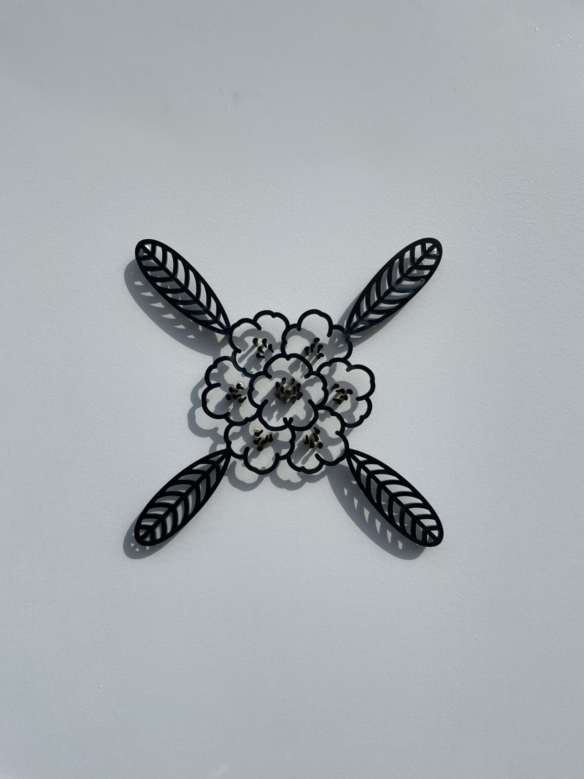 Black metal sculpture of a yakushima shakunage rhododendron flower mounted on a white wall
