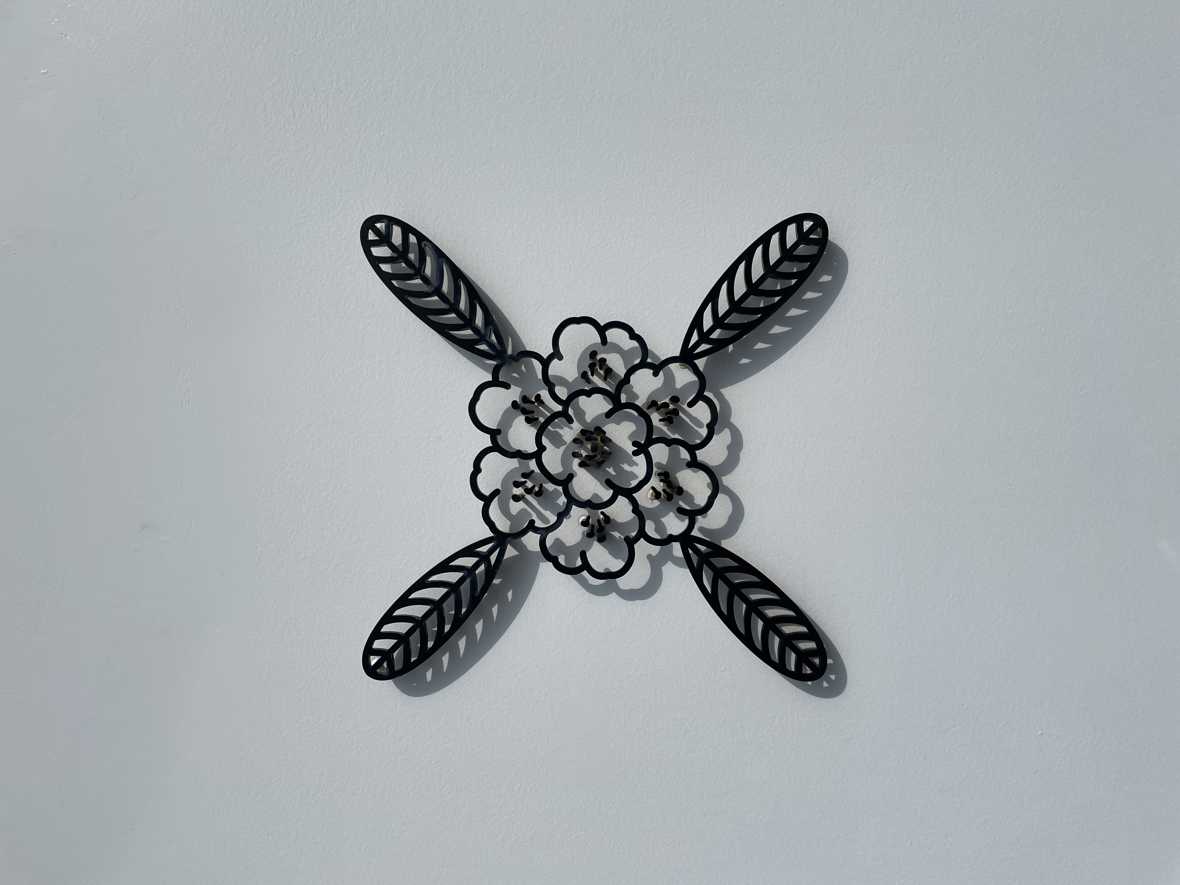 Black metal sculpture of a yakushima shakunage rhododendron flower mounted on a white wall