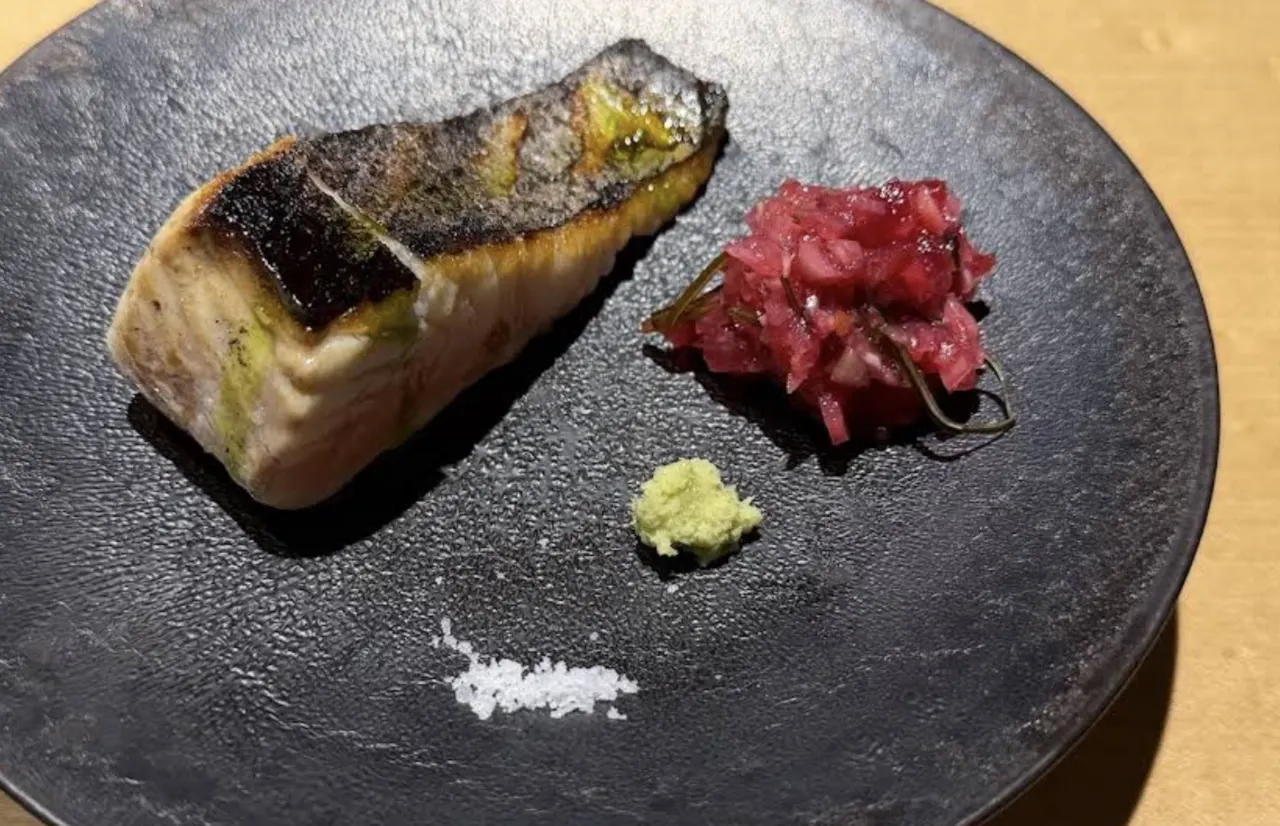 Grilled fish at TOAHIS Fukuoka with crispy skin, served on a black plate with pickled red onion, wasabi paste, and sea salt