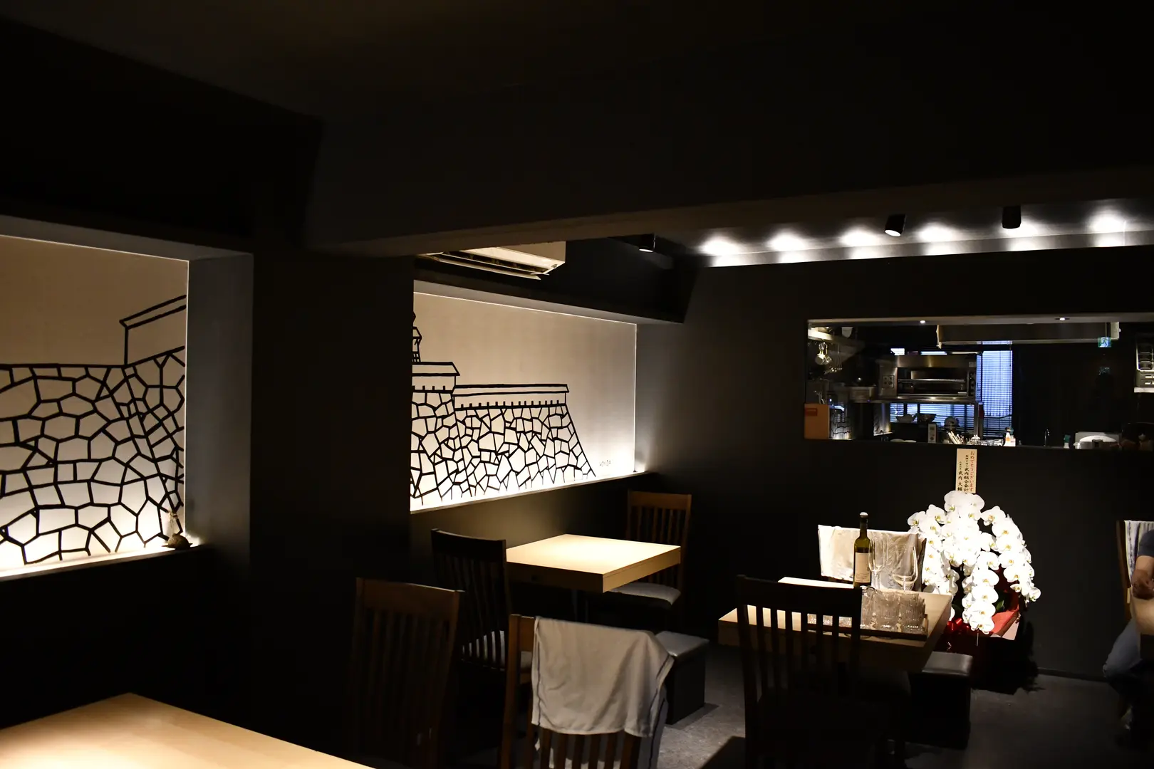 Wider view of TOAHIS dining room showing the open kitchen, multiple tables, and white orchid arrangement