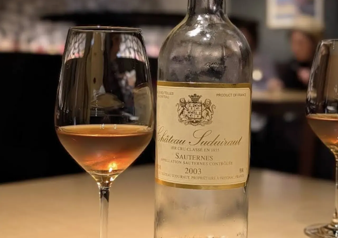 A 2003 Château Suduiraut Sauternes wine bottle on the TOAHIS bar with a glass of golden dessert wine in the foreground