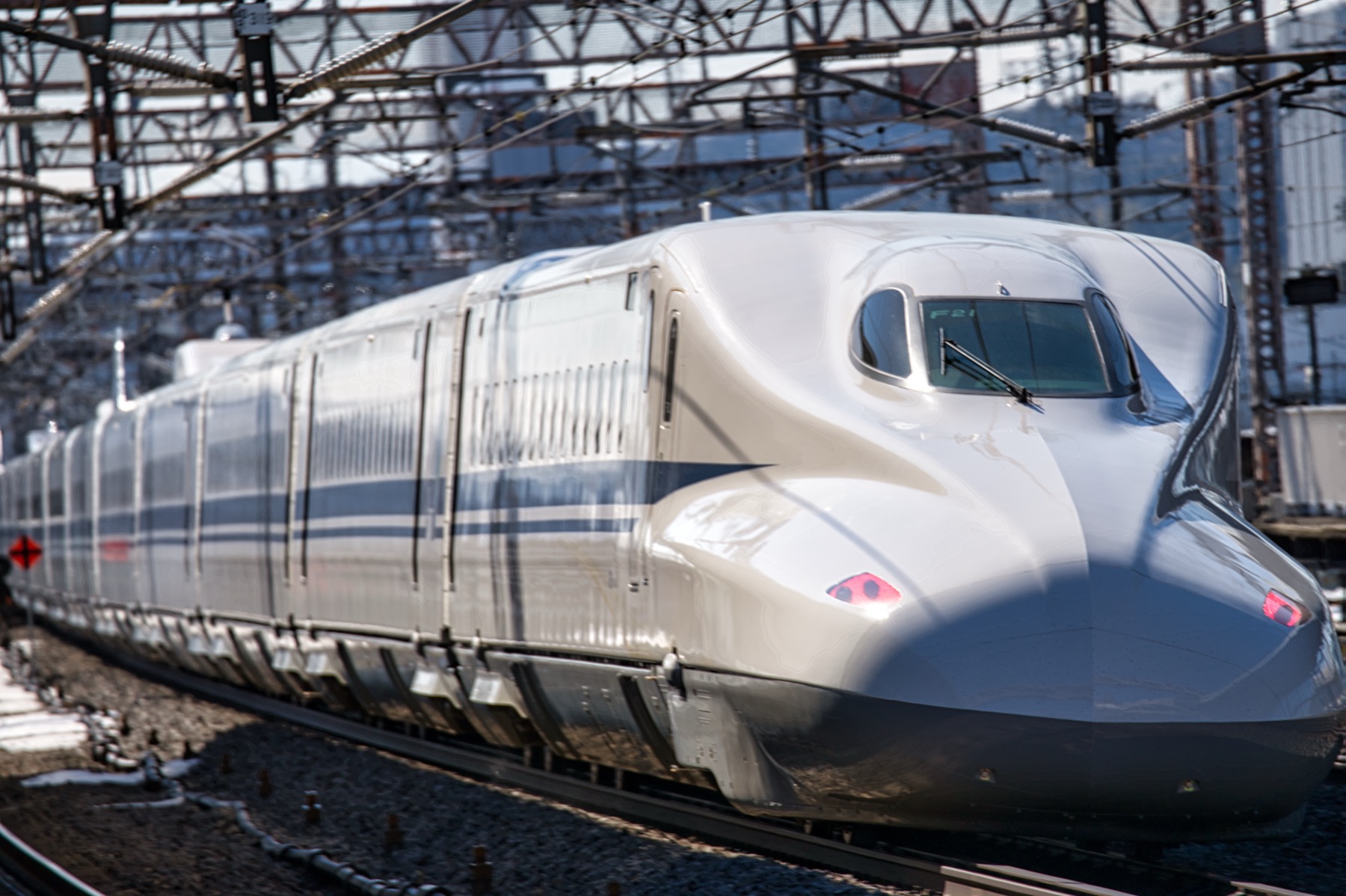 Front nose of a white N700 Series Tokaido Shinkansen bullet train approaching the platform on a winter morning with snow on the ground beside the tracks