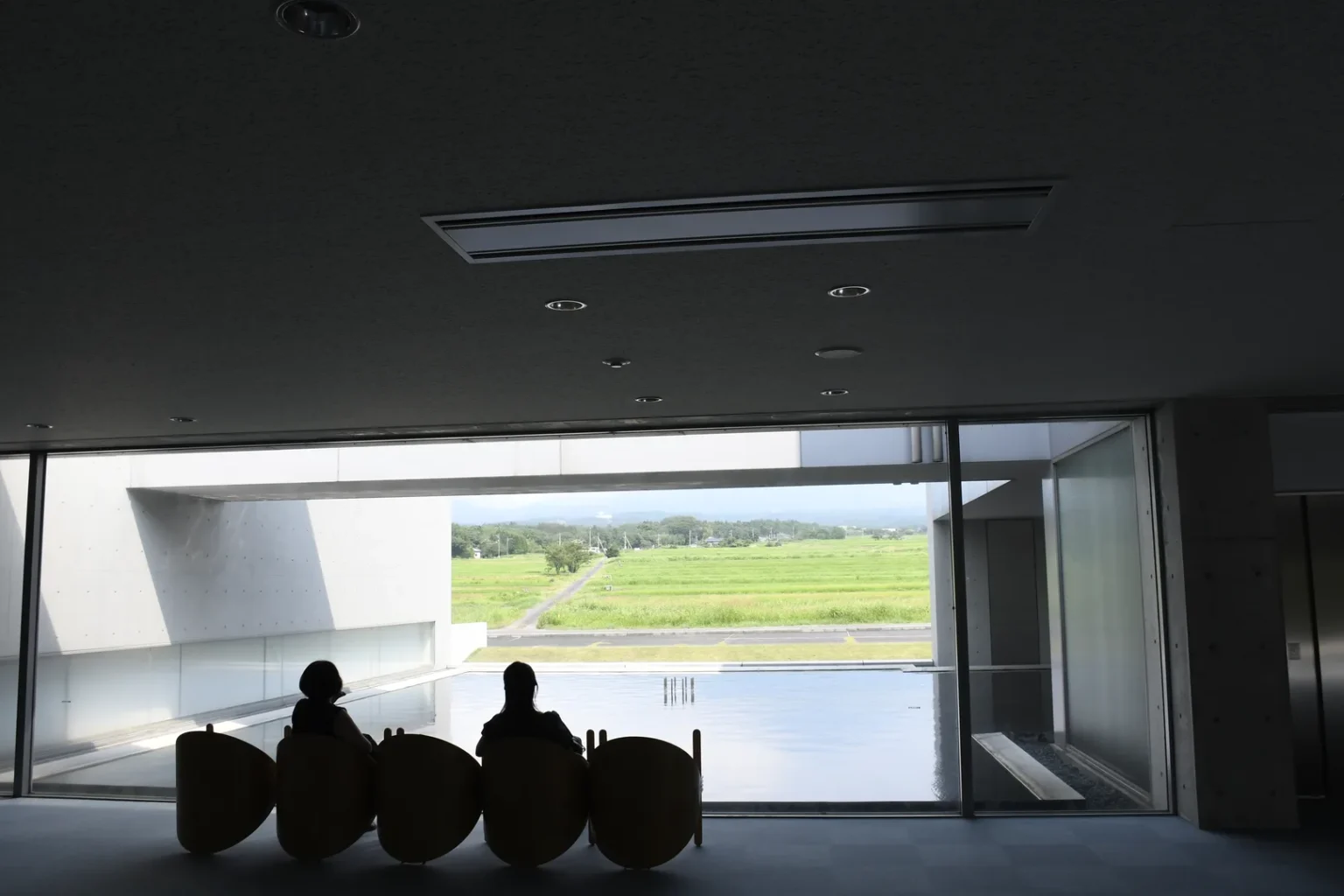 Visitors sitting in egg-shaped pod chairs in the indoor lounge of Shoji Ueda Museum facing the reflecting pool and Mt Daisen view