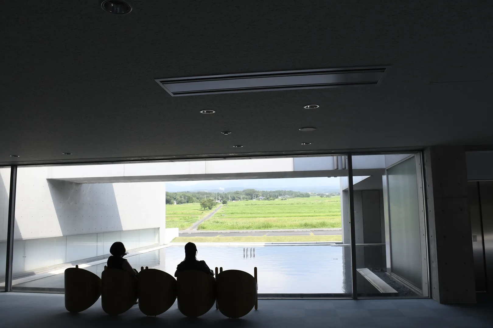 Visitors sitting in egg-shaped pod chairs in the indoor lounge of Shoji Ueda Museum facing the reflecting pool and Mt Daisen view