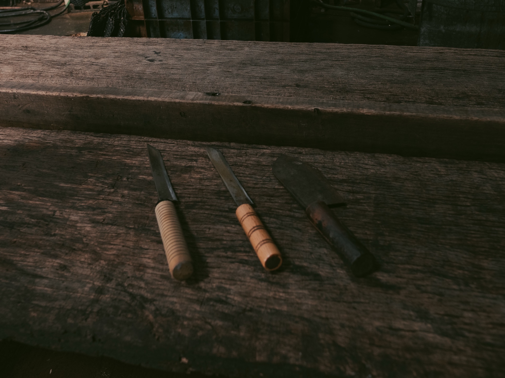 Three traditional Japanese craftsman knives lined up on a wooden bench at the Yamaju workshop