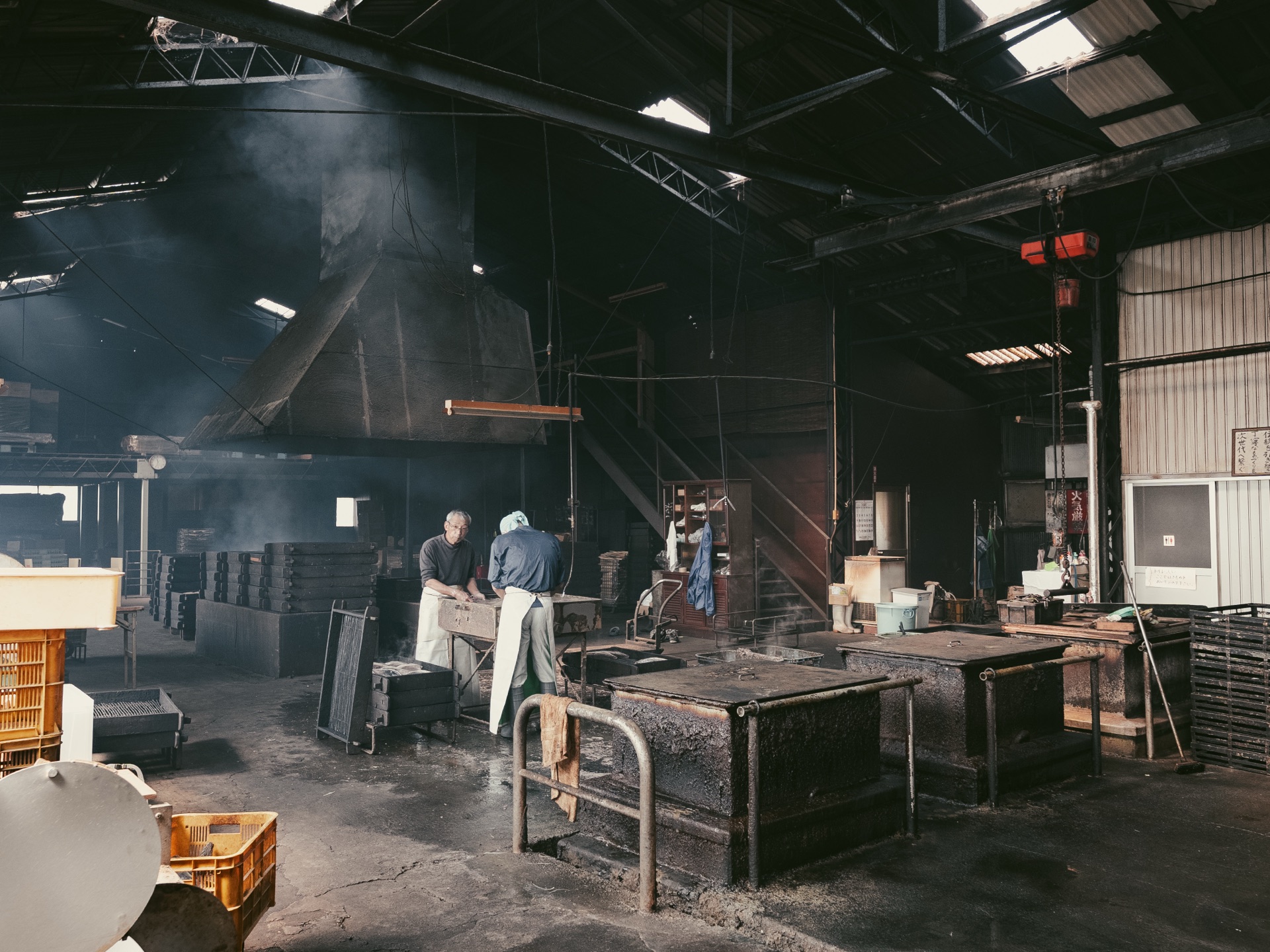 Two craftsmen working side by side at a smoking station in the dark workshop with steam rising