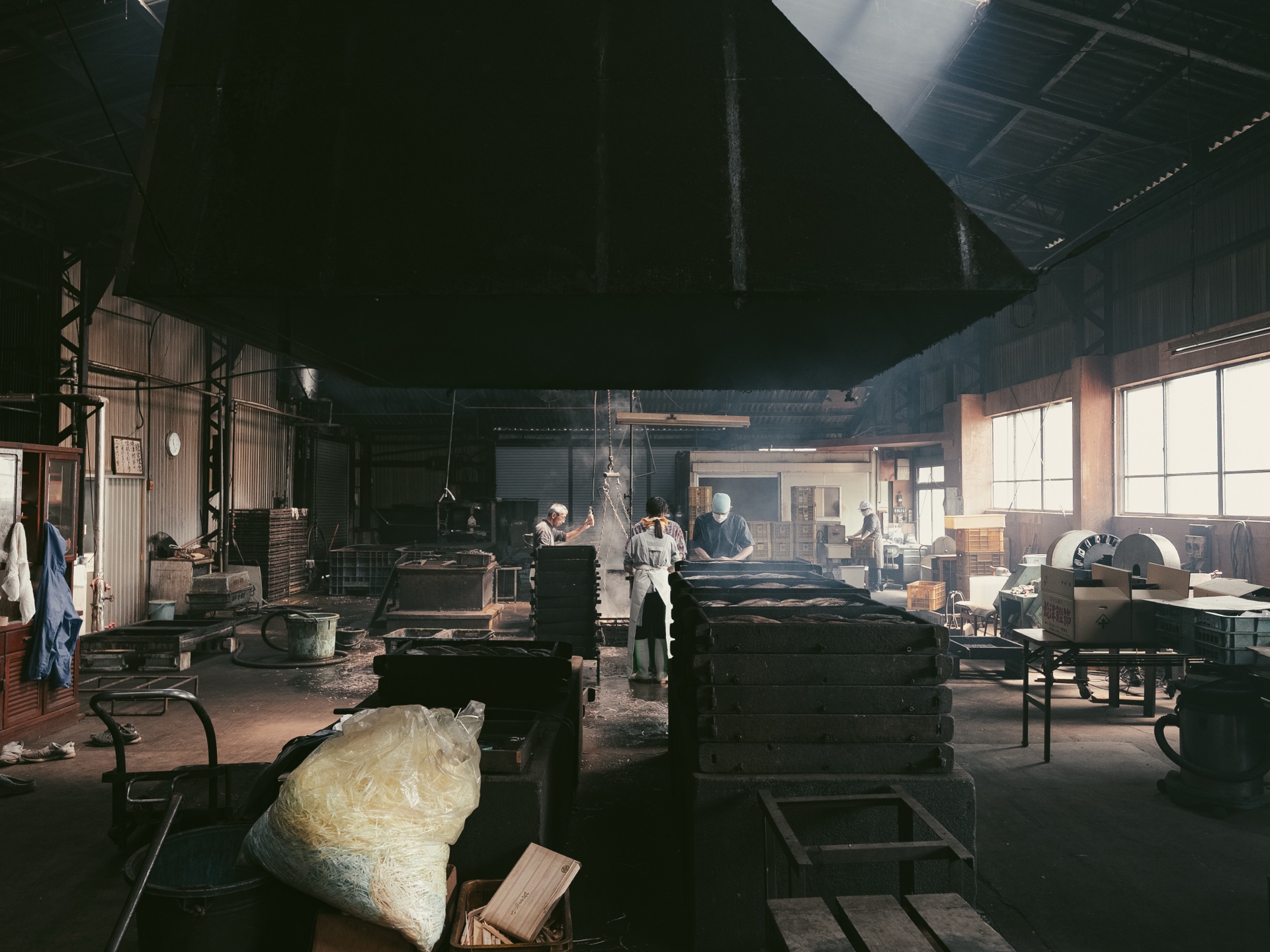 Three craftsmen working in the dark interior of the Yamaju workshop with smoke and steam visible