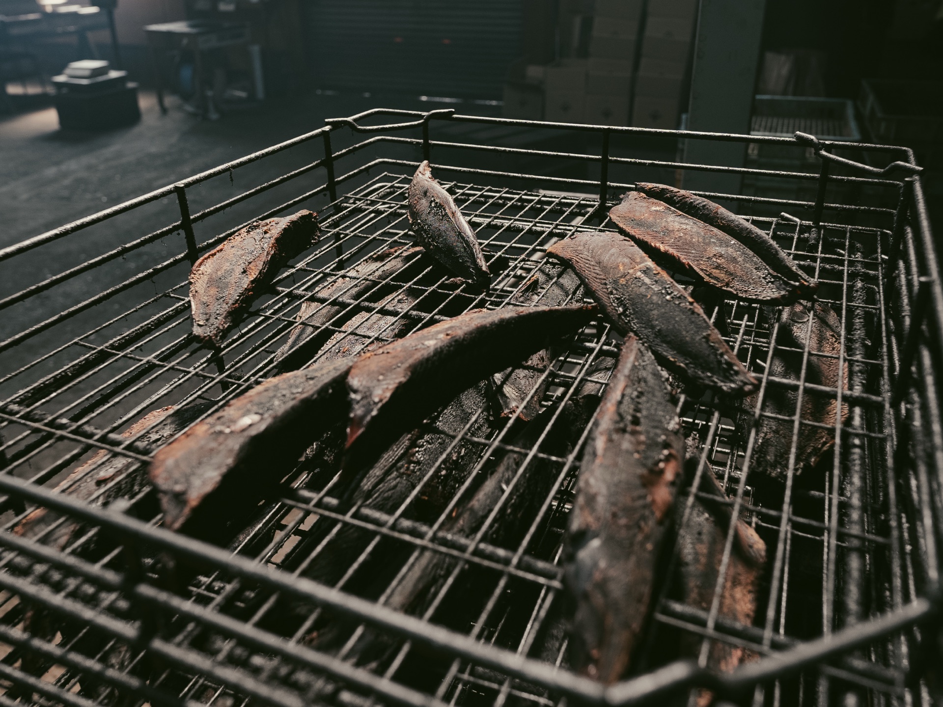 Deeply smoked bonito loins on an iron grate showing the dark mahogany surface from repeated smoking cycles