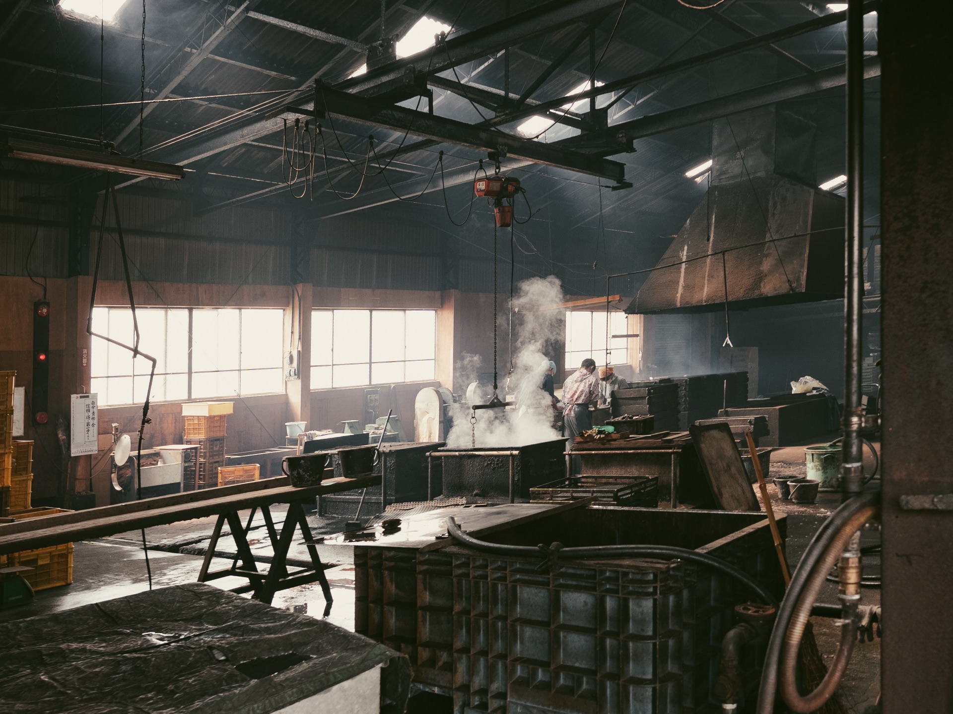 Wide view of the Yamaju katsuobushi factory interior with steam rising from a smoking station and a craftsman working at the back