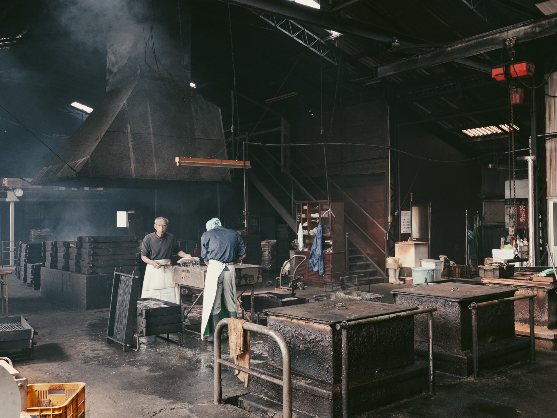 Two craftsmen at the finishing stage of katsuobushi production at Yamaju in the dark smoky workshop