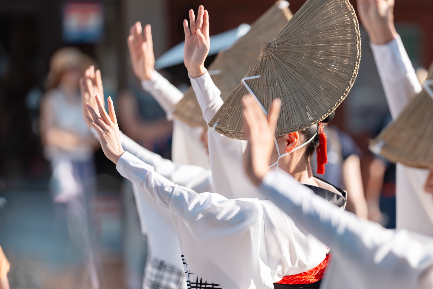 Awa Odori dancers in white summer kimono and woven amigasa straw hats with their arms raised mid-dance in the street at the Tokushima dance festival in August