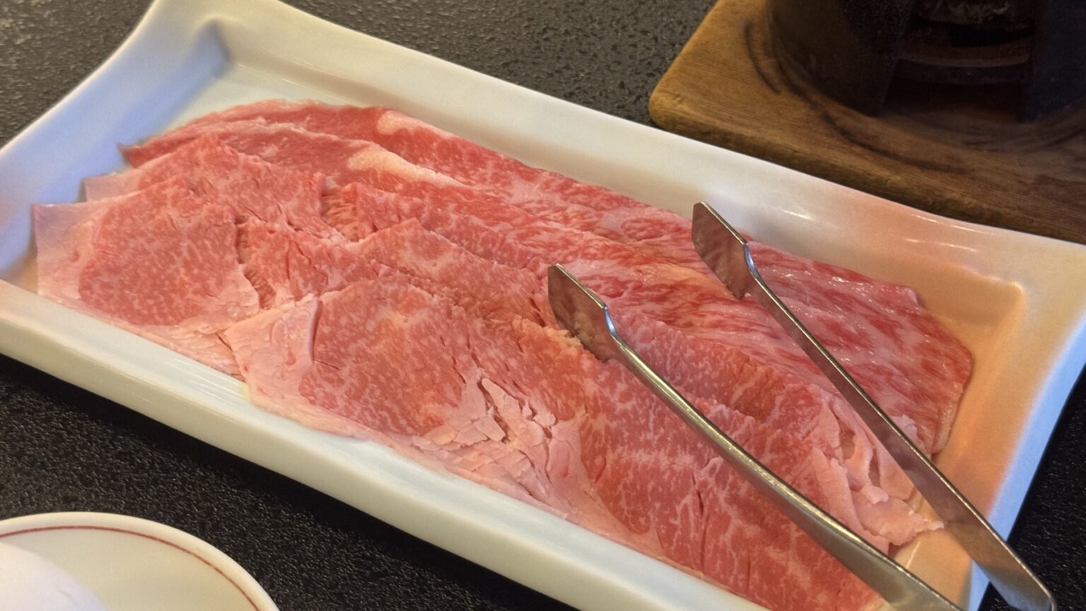 A long white plate of thinly sliced, well-marbled domestic Japanese beef with serving tongs, prepared for shabu-shabu or sukiyaki at Club Wyndham Chikumakan, Nagano