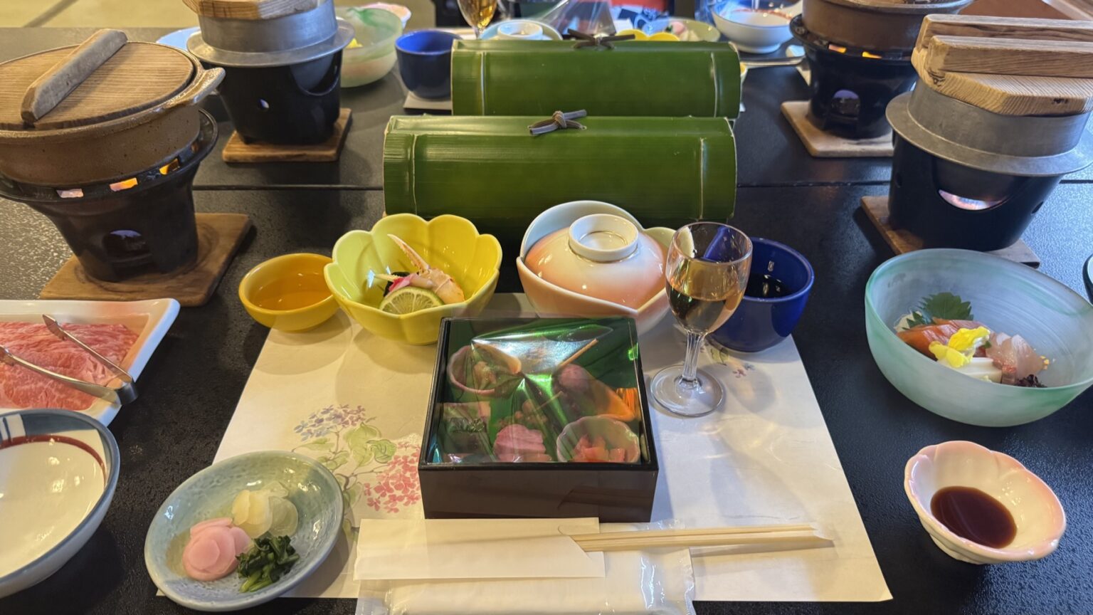 A multi-course kaiseki dinner spread at Club Wyndham Chikumakan with individual tabletop hot-pot burners, a lacquer box, small bowls, sashimi and a glass of wine, in Togura-Kamiyamada Onsen, Nagano