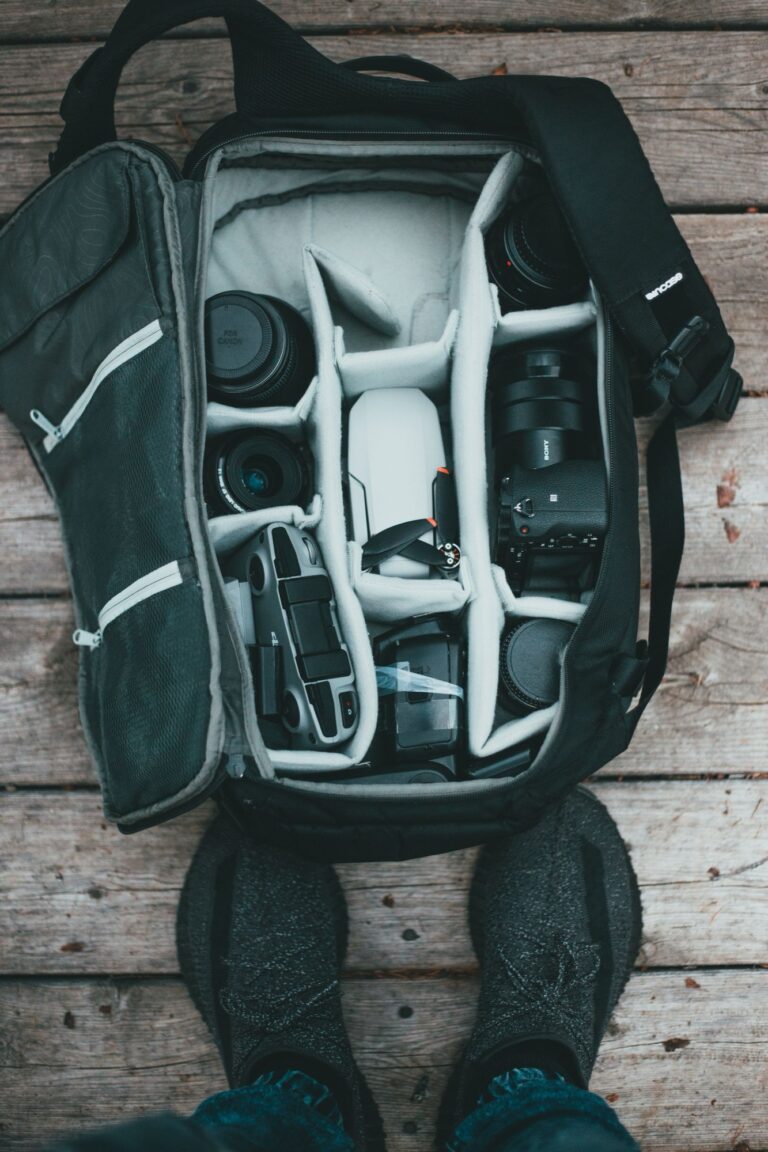 A camera backpack opened from above on weathered wood, packed with a mirrorless body, two lenses, a small drone and accessories slotted into padded dividers, ready for a day of travel shooting in Japan.