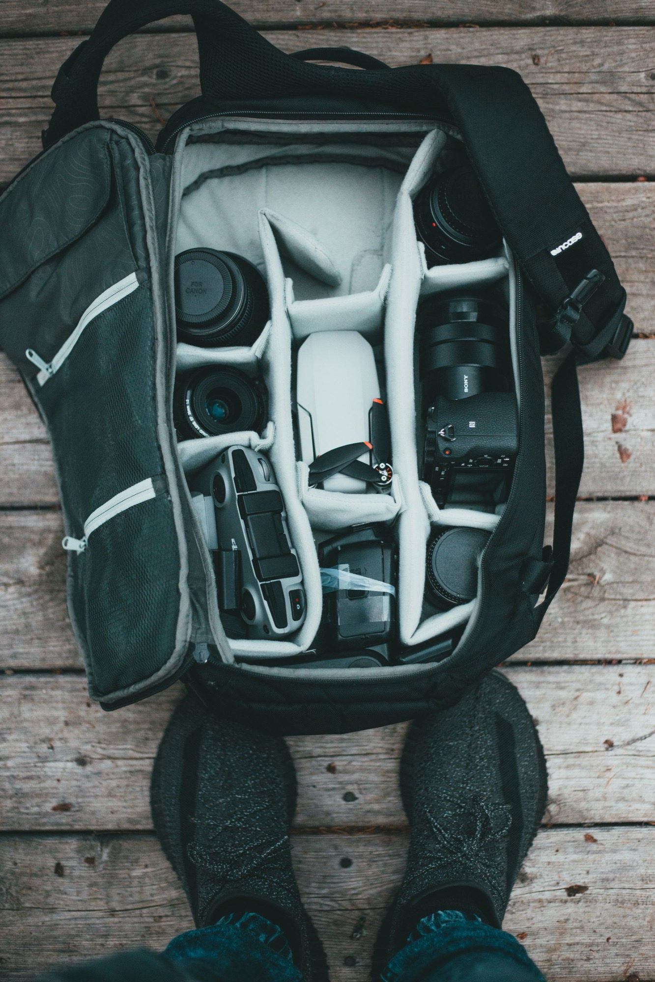A camera backpack opened from above on weathered wood, packed with a mirrorless body, two lenses, a small drone and accessories slotted into padded dividers, ready for a day of travel shooting in Japan.