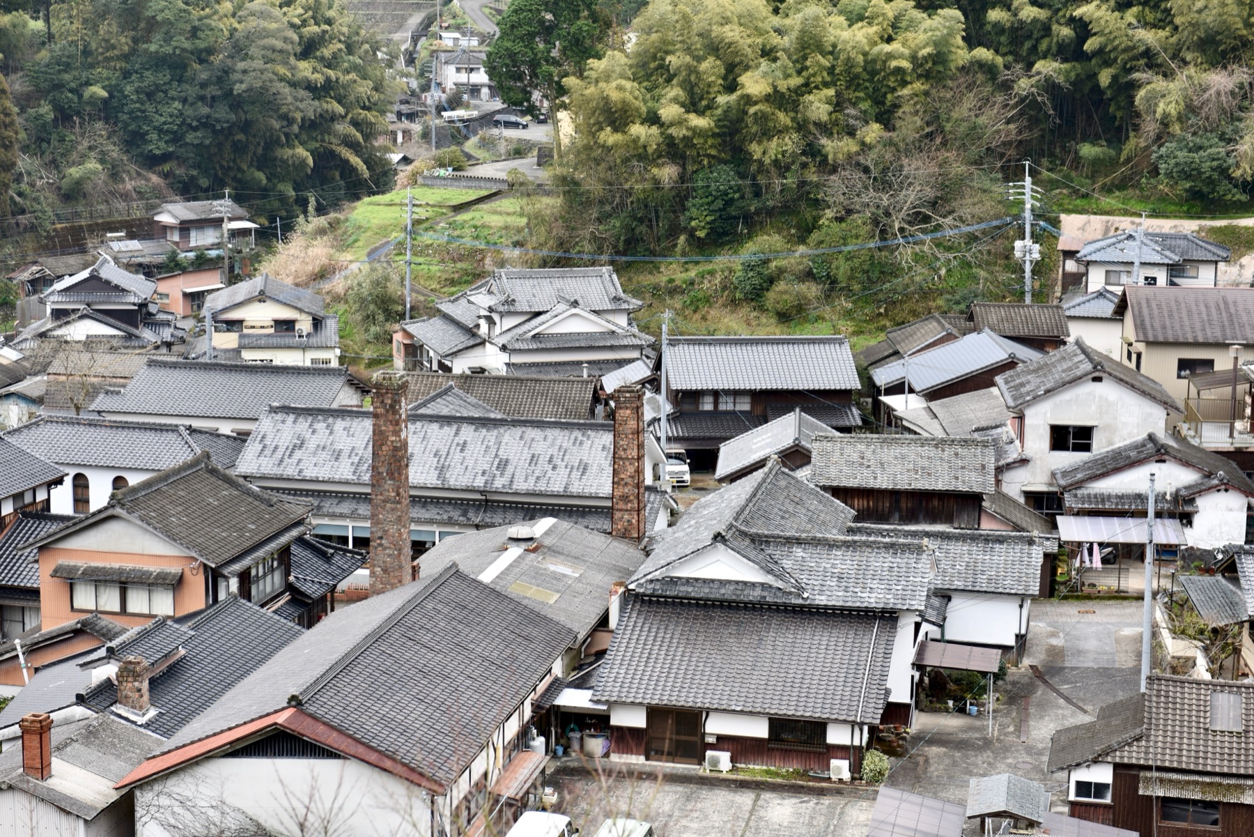 An elevated view of a traditional Japanese village of tiled-roof houses with tall brick kiln chimneys rising among them, a historic porcelain kiln village in the Imari area of Saga