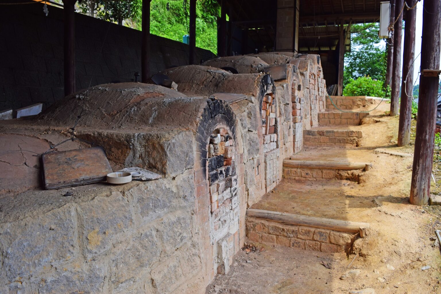 A row of old brick climbing-kiln chambers stepping up a hillside under a shelter