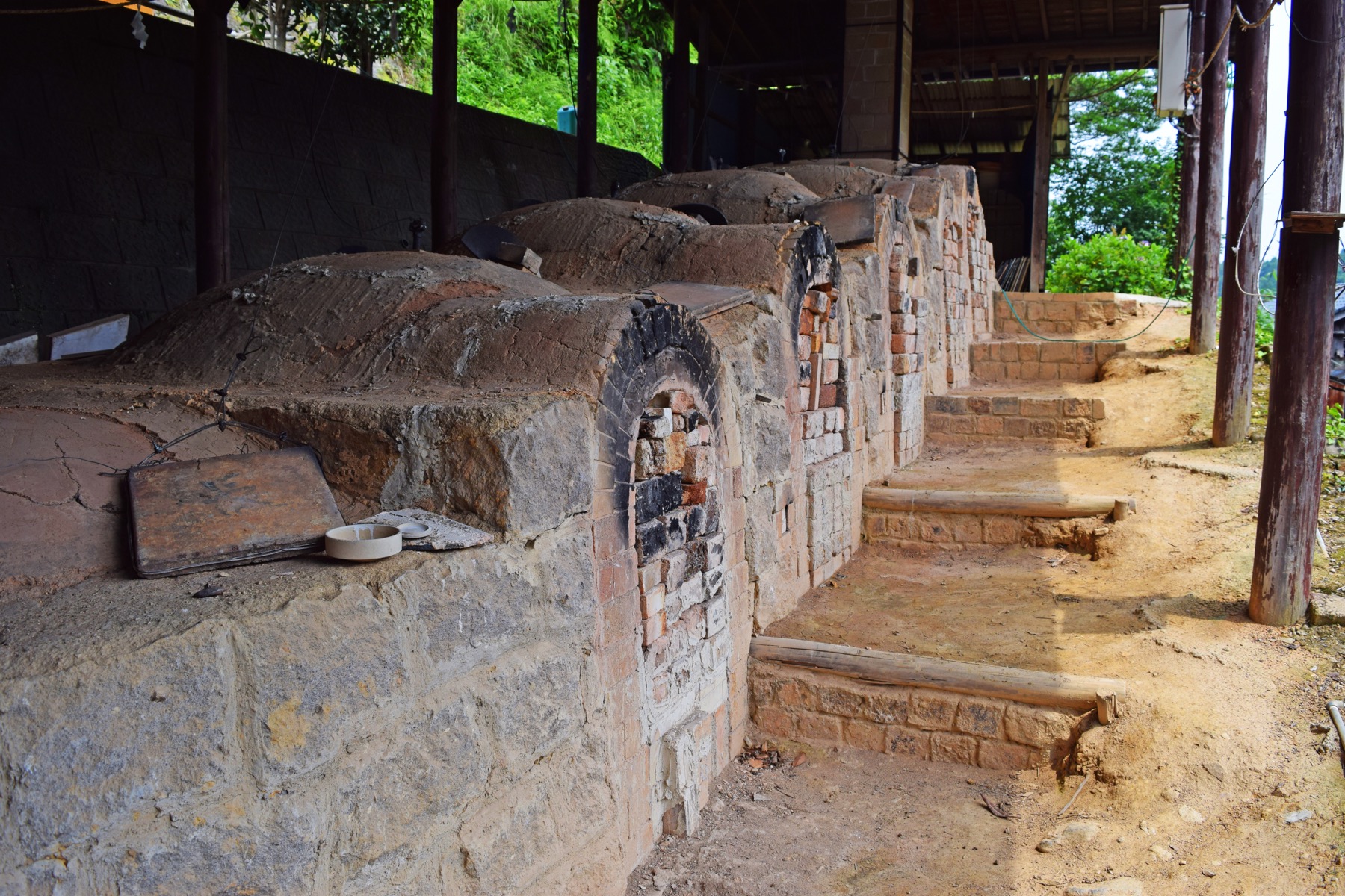 A row of old brick climbing-kiln (noborigama) chambers stepping up a hillside under a shelter, the wood-fired multi-chamber kilns once used to fire Imari and Arita porcelain in Saga