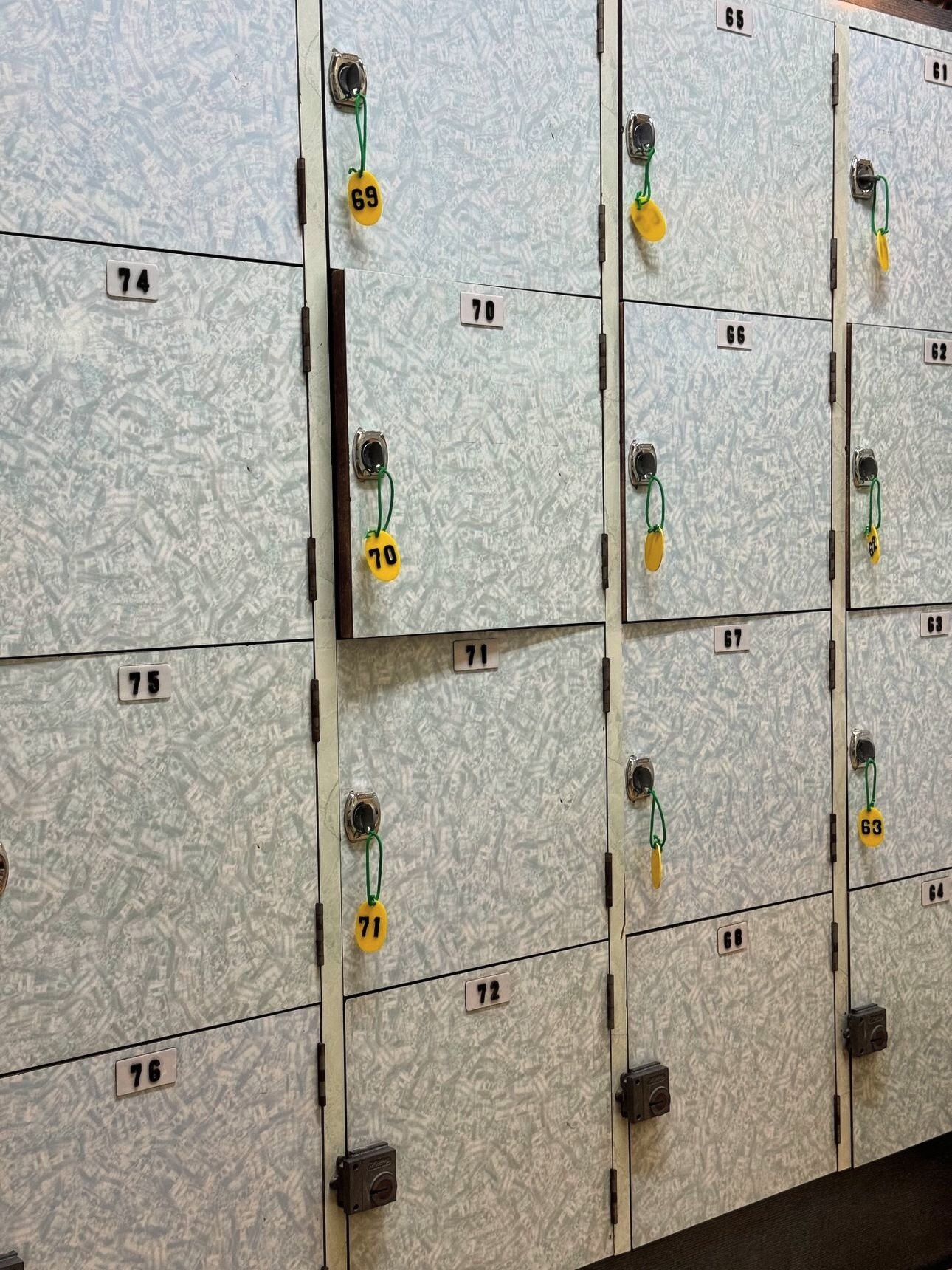 A wall of wooden changing-room lockers in a Japanese sentō, each with a number and a yellow key tag on a green coil.