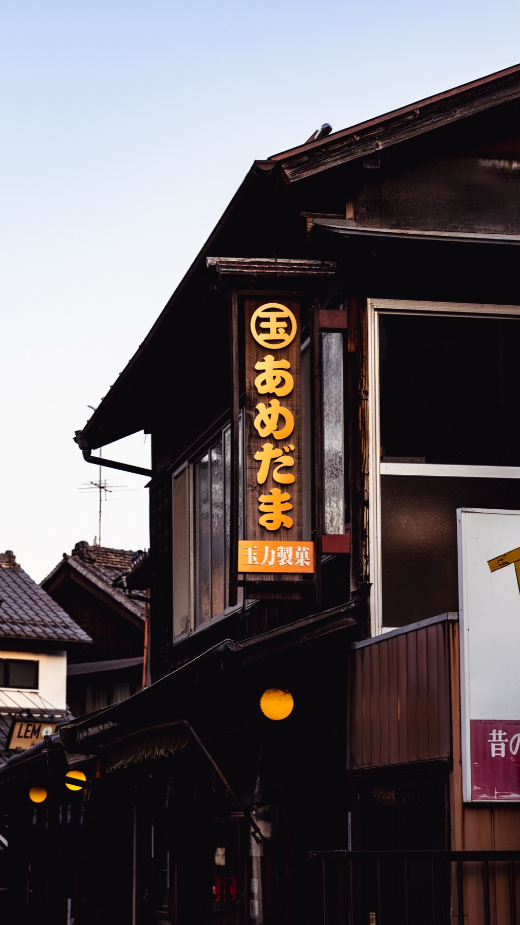 An old candy shop in Kawagoe's Kashiya Yokocho candy alley, with a glowing orange lantern sign reading あめだま above a dark timber storefront at dusk.
