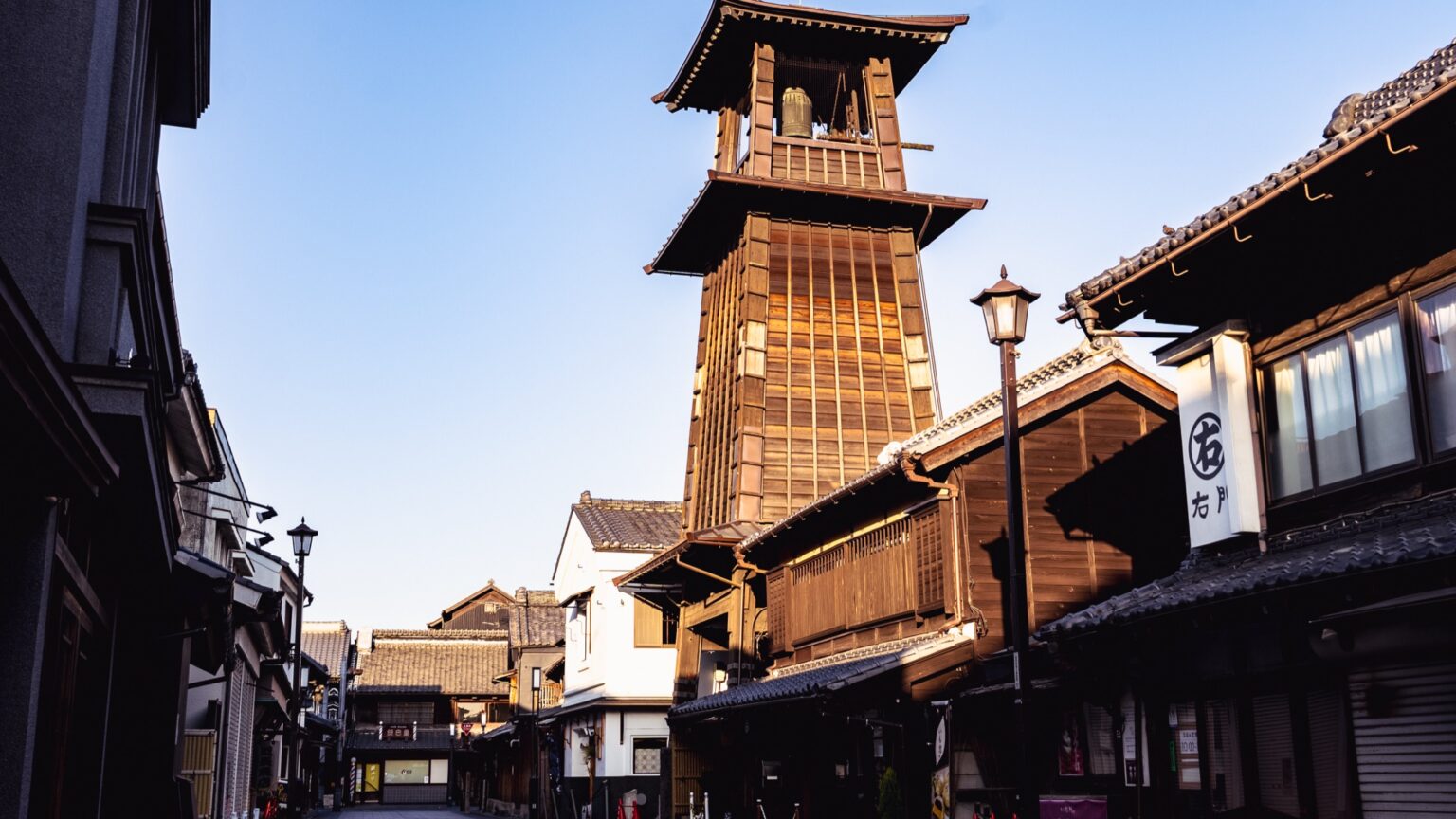 The wooden Toki no Kane bell tower of Kawagoe glowing in golden-hour light above the tiled roofs of the old merchant quarter.
