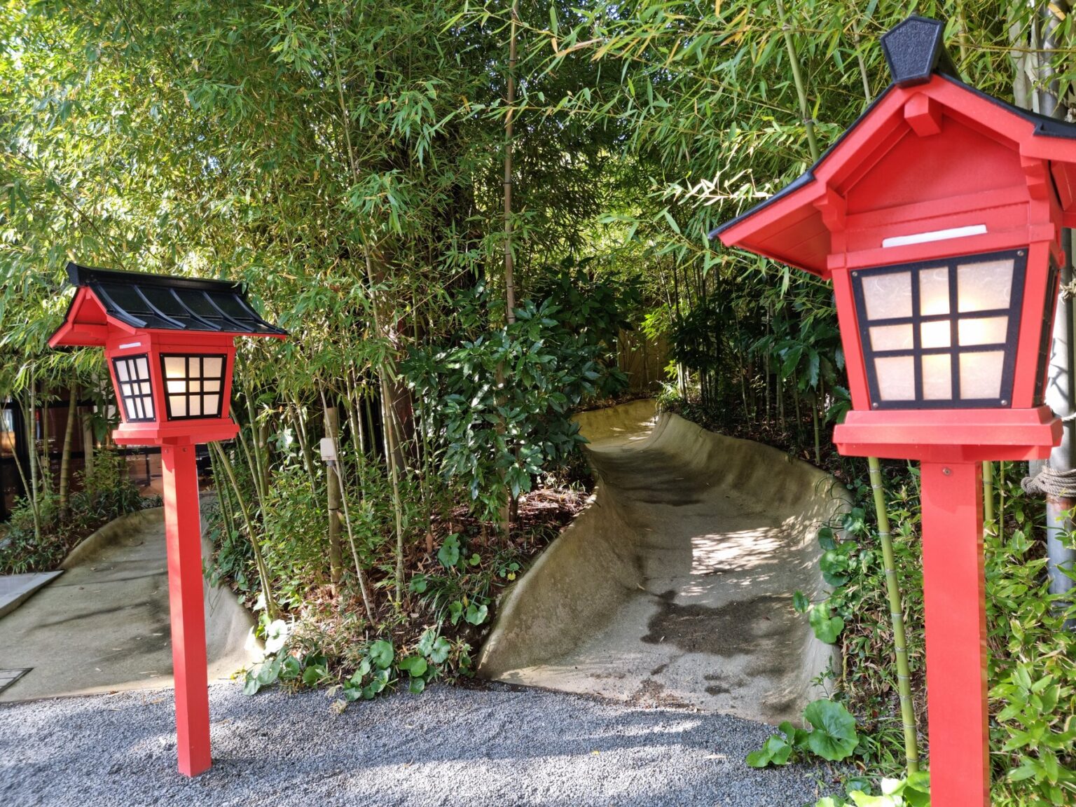 Two red wooden lanterns flanking a curved stone path through a green bamboo grove on the grounds of Kinomiya Shrine in Atami.