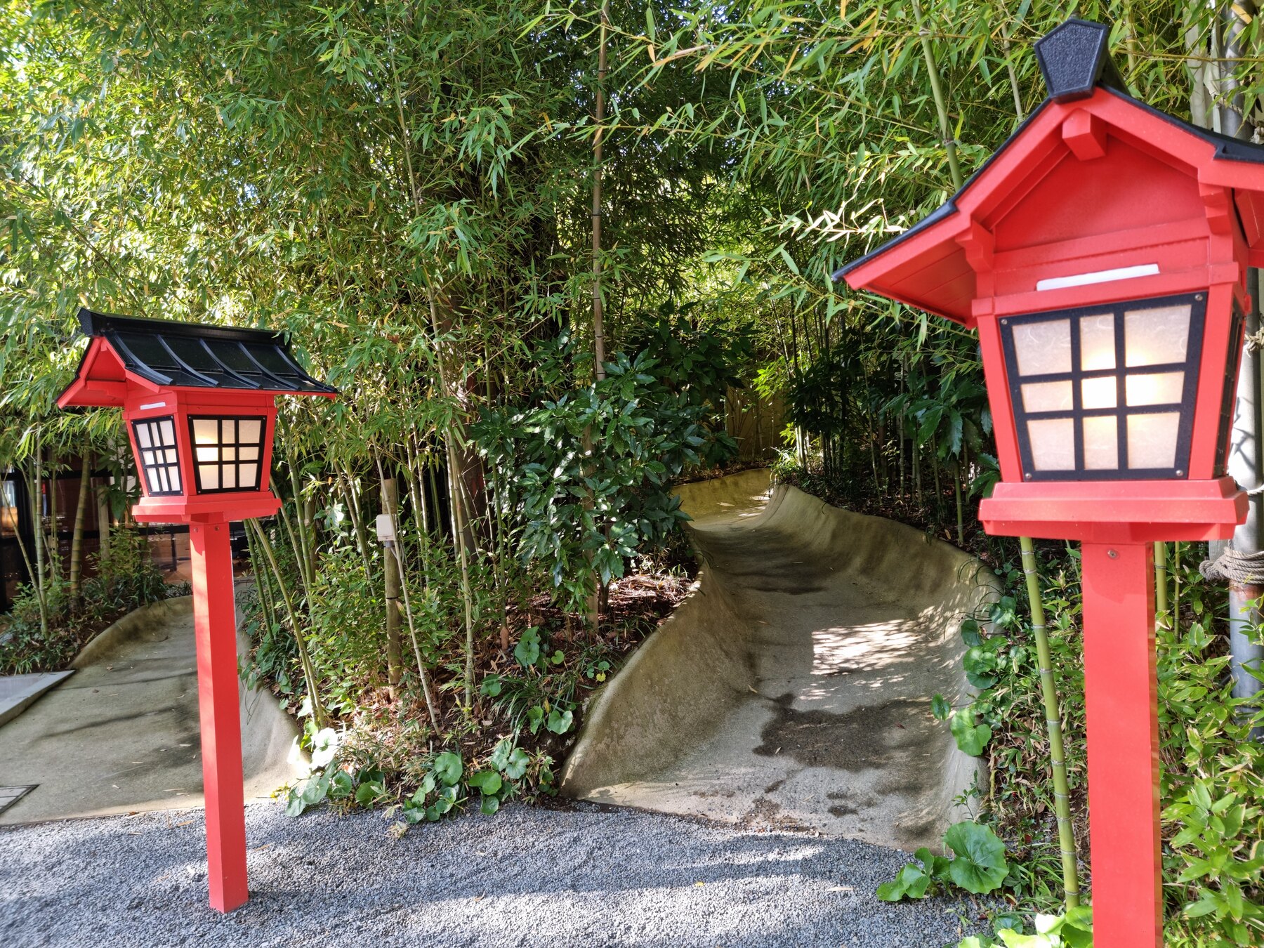 Two red wooden lanterns flanking a curved stone path through a green bamboo grove on the grounds of Kinomiya Shrine in Atami.