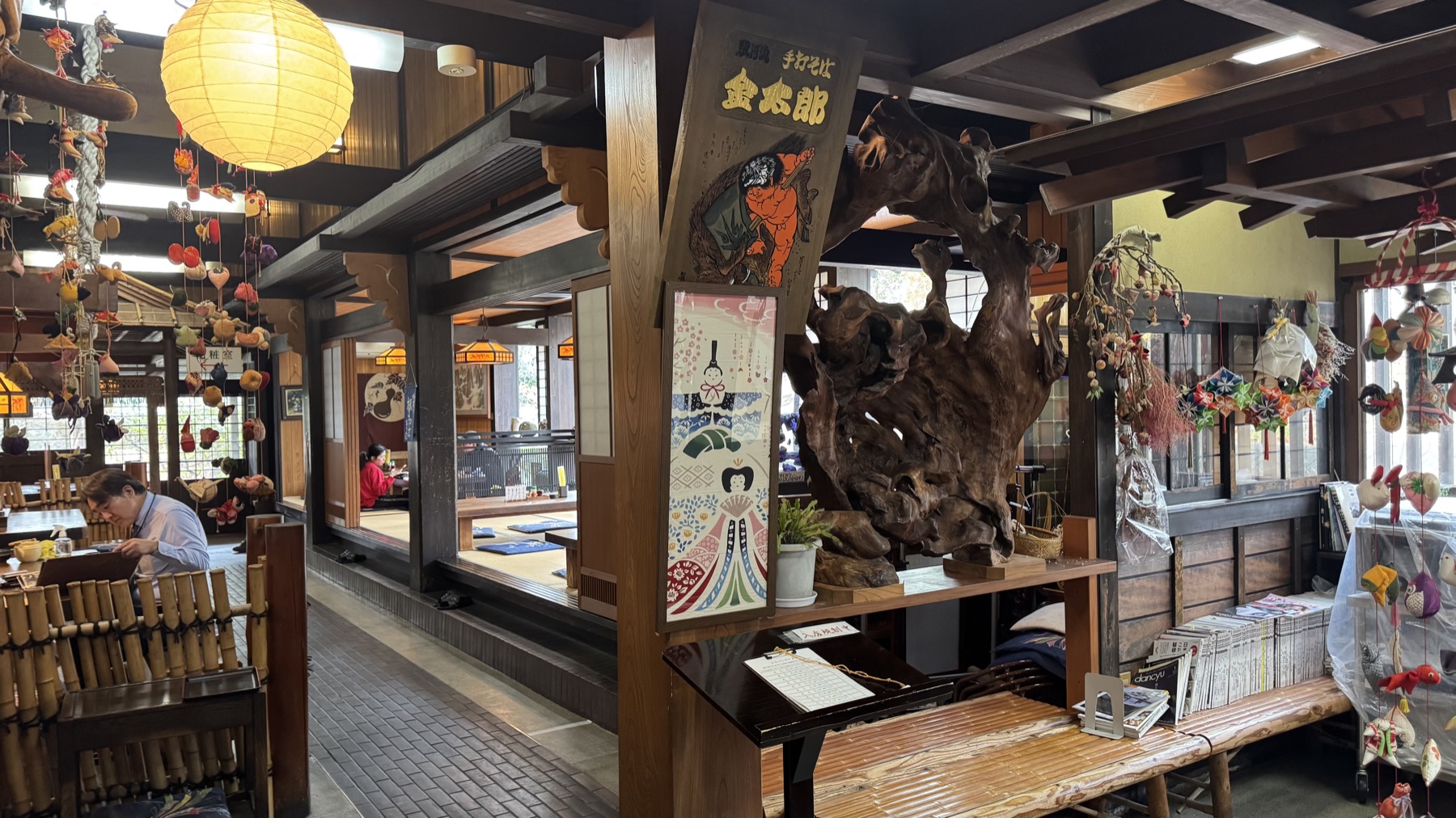 The old-farmhouse interior of Kintaro soba house in Gotemba, with a Kintaro banner, a large polished tree-root display and hanging seasonal decorations over a timber dining room