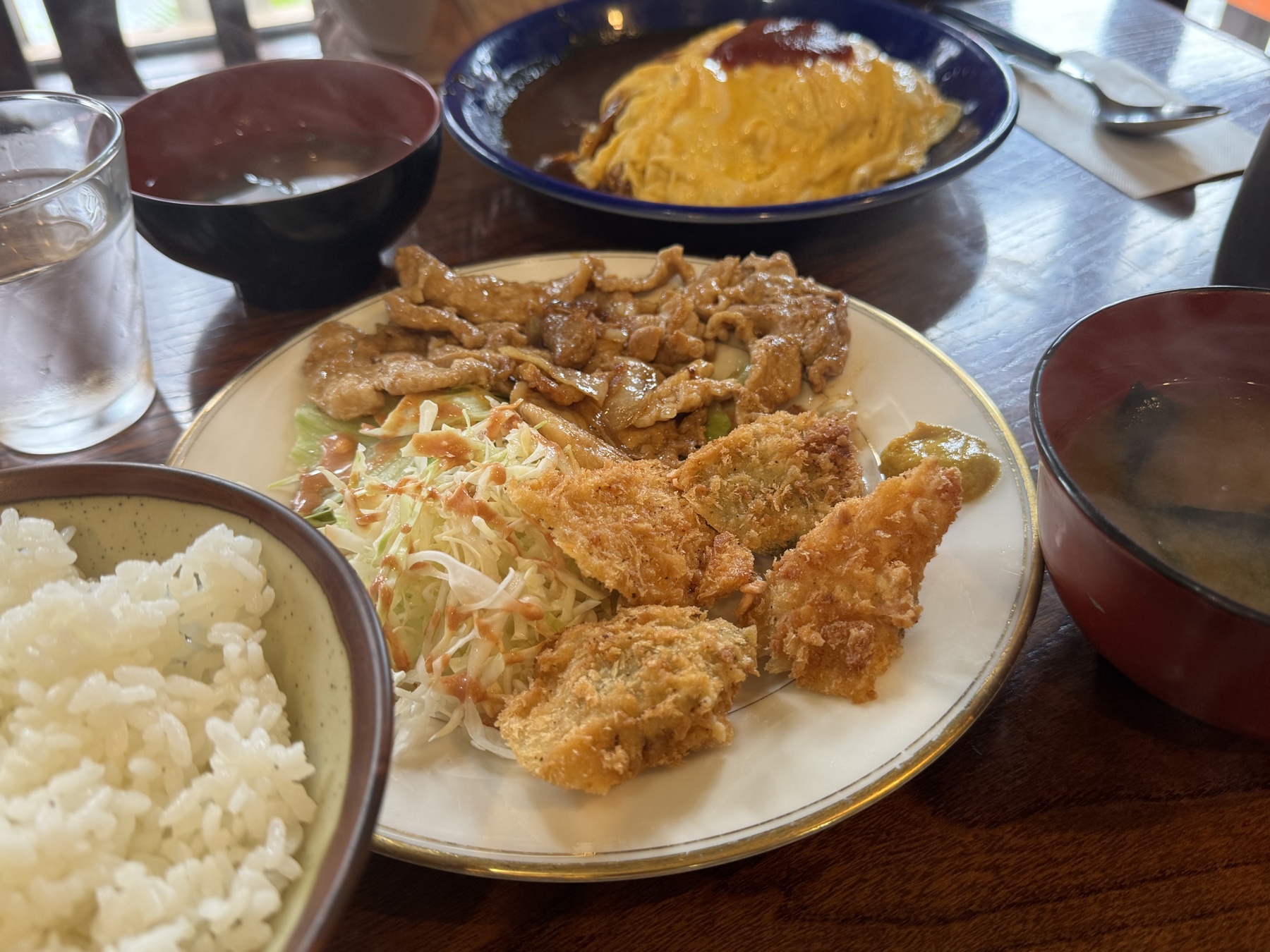 A set-meal plate at a Japanese diner with strips of ginger-grilled pork and fried chicken cutlet pieces over shredded cabbage, served with a bowl of white rice and miso soup.